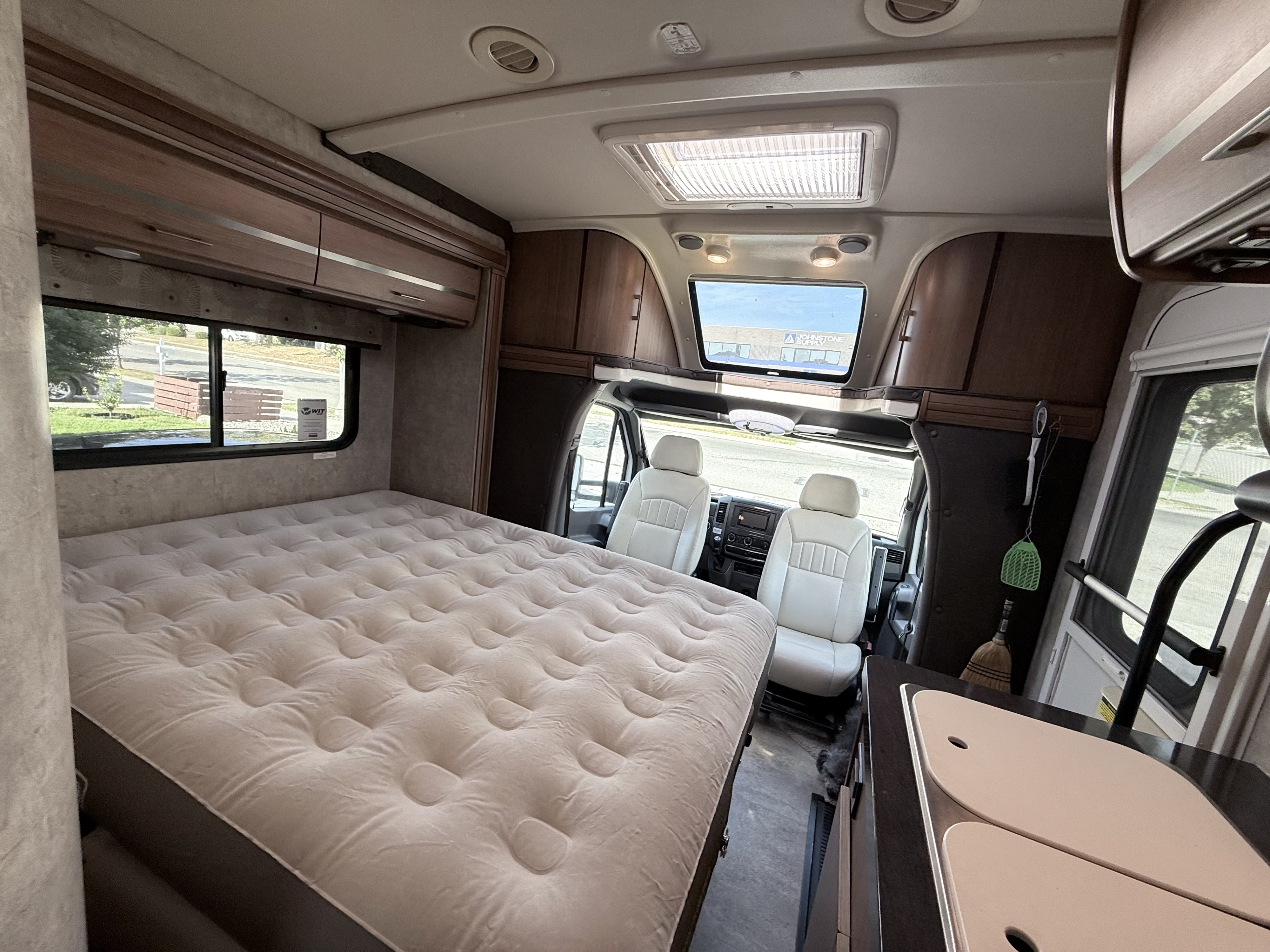 Inside this rv rental: a large, tufted bed, front cockpit with cream seats, and a small kitchen counter with sink covers.. Winnebago View 2015