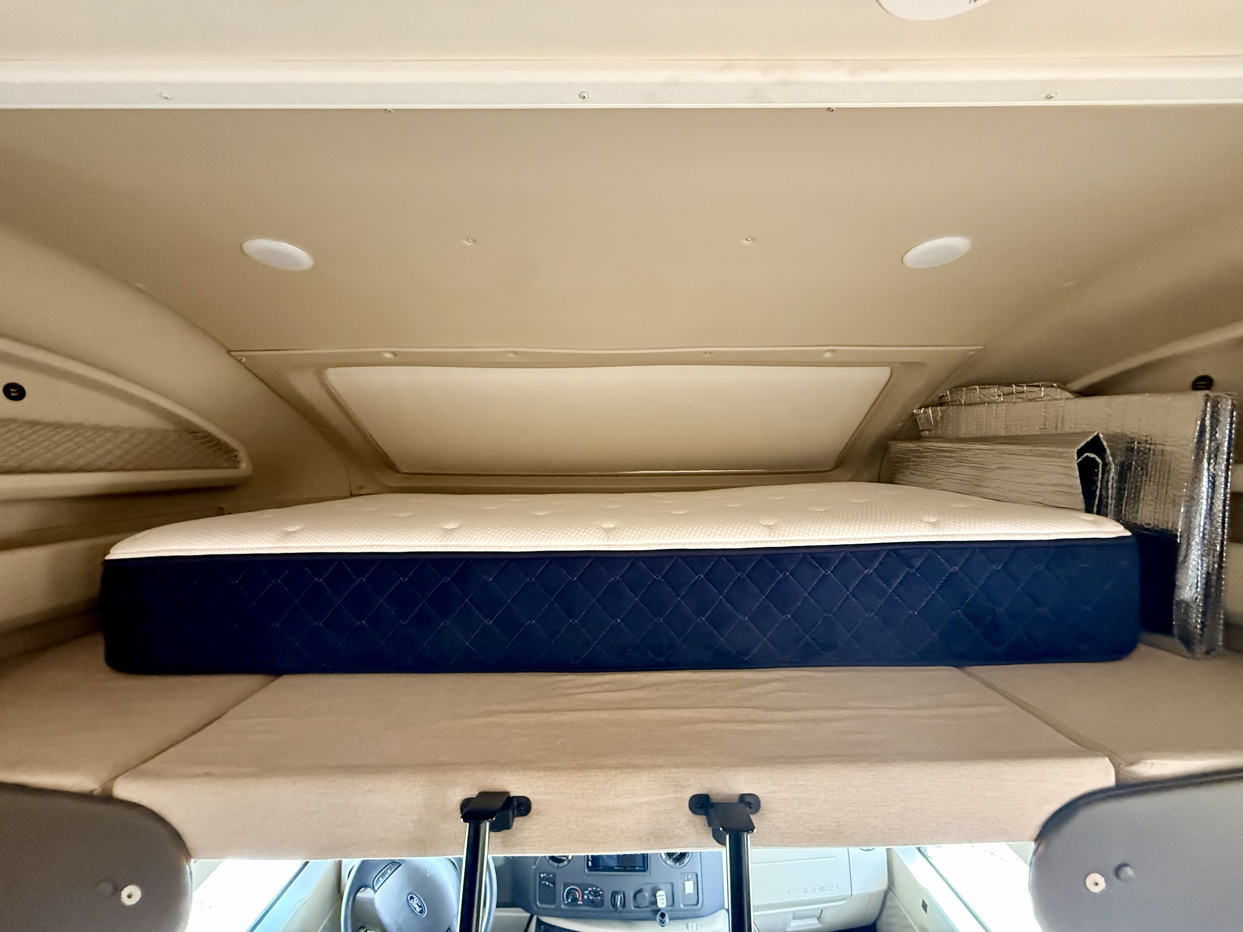 Spacious overhead bunk bed with a comfy mattress in an RV rental. Storage pockets visible, cockpit below.. Entegra Coach Odyssey 2020
