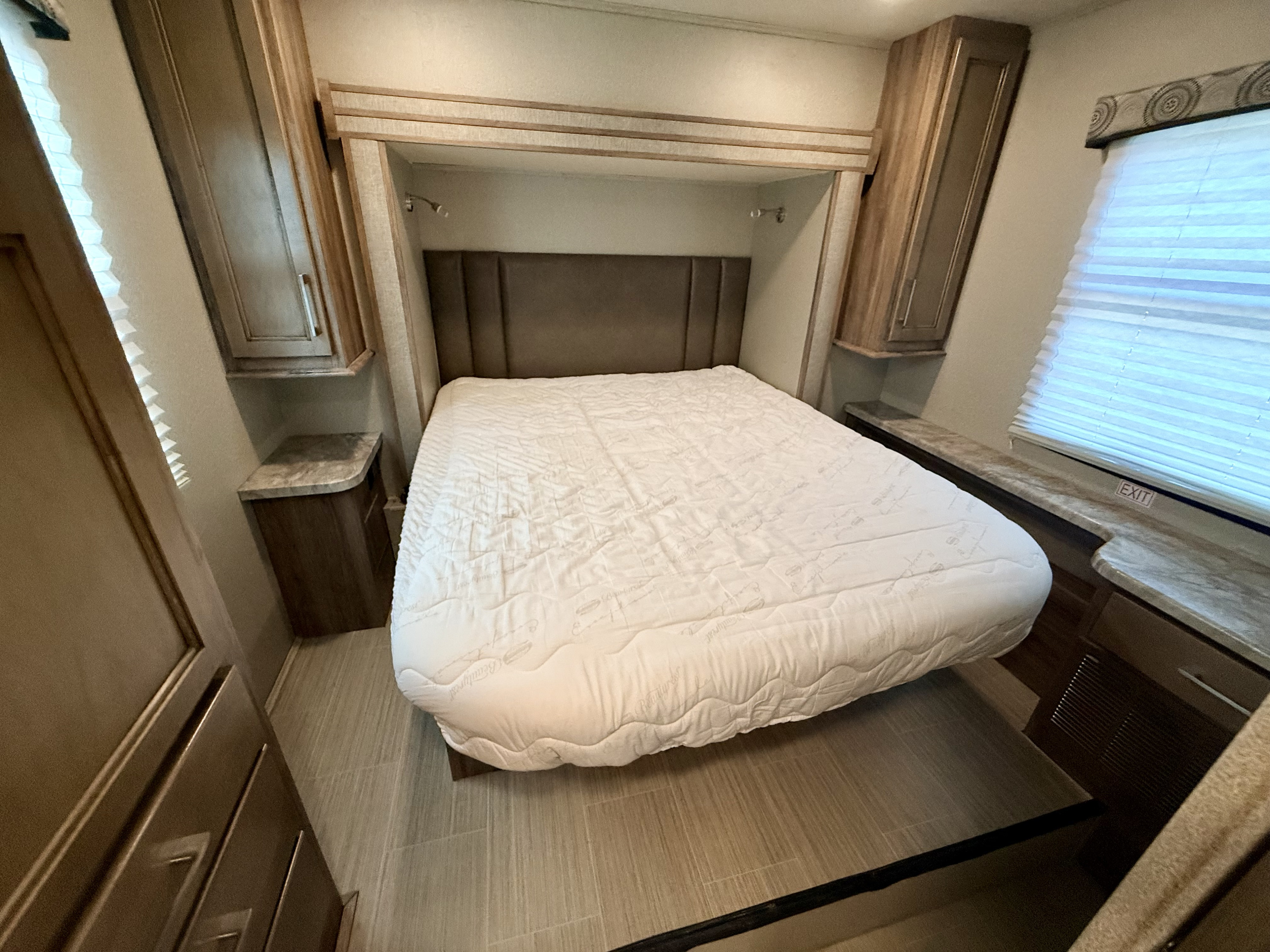 Comfortable RV rental bedroom featuring a large bed, built-in cabinets, and a window, offering a cozy travel space.. Entegra Coach Odyssey 2020