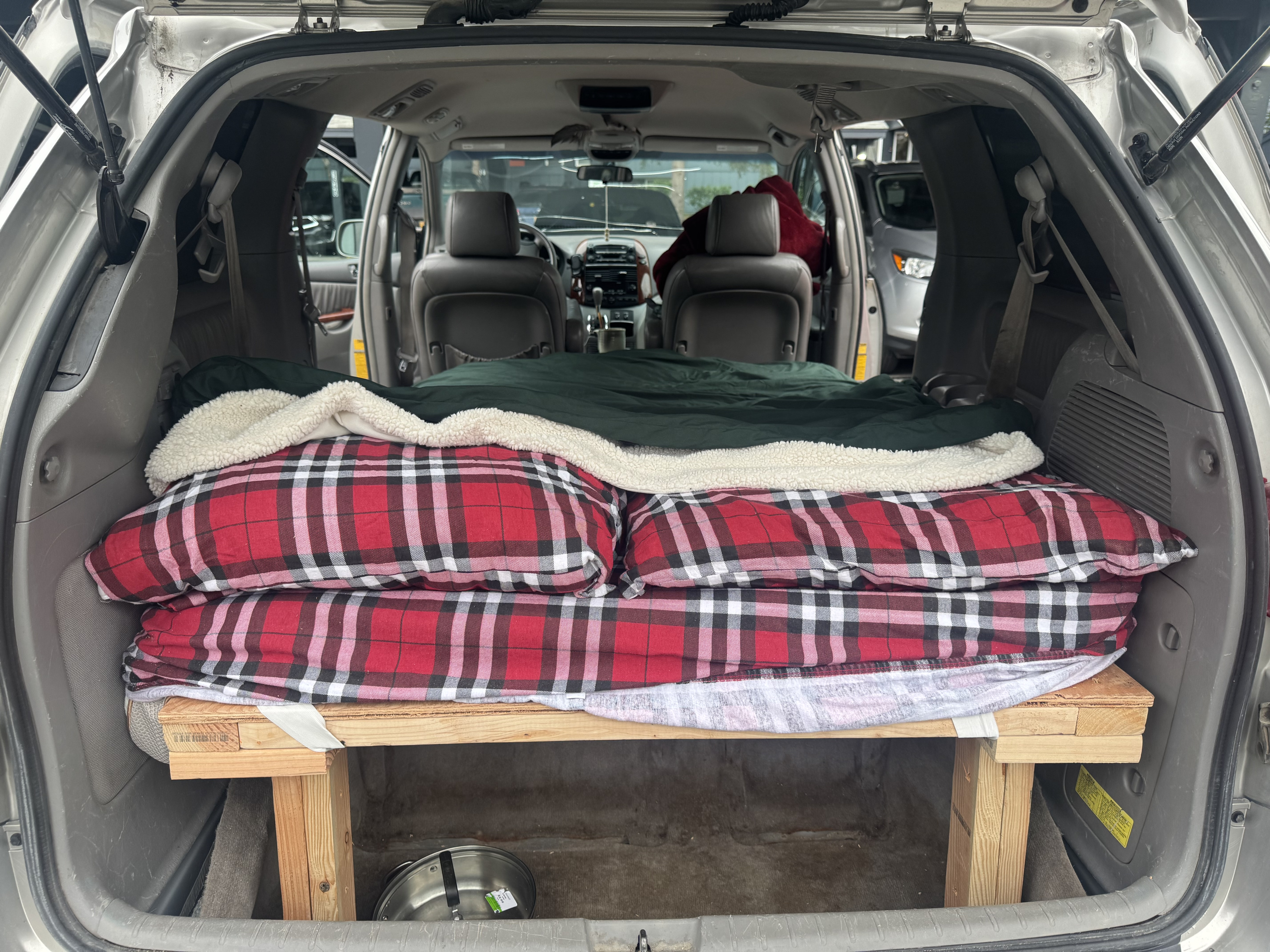 Inside a minivan, a DIY wooden bed platform with plaid bedding offers a cozy sleep setup, great for an RV rental alternative.. Toyota Toyota Sienna XLE 2005