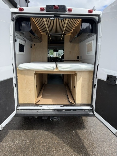 RV rental campervan interior from the rear, featuring two beds with white mattresses & wood storage.. Safari Safari 2025