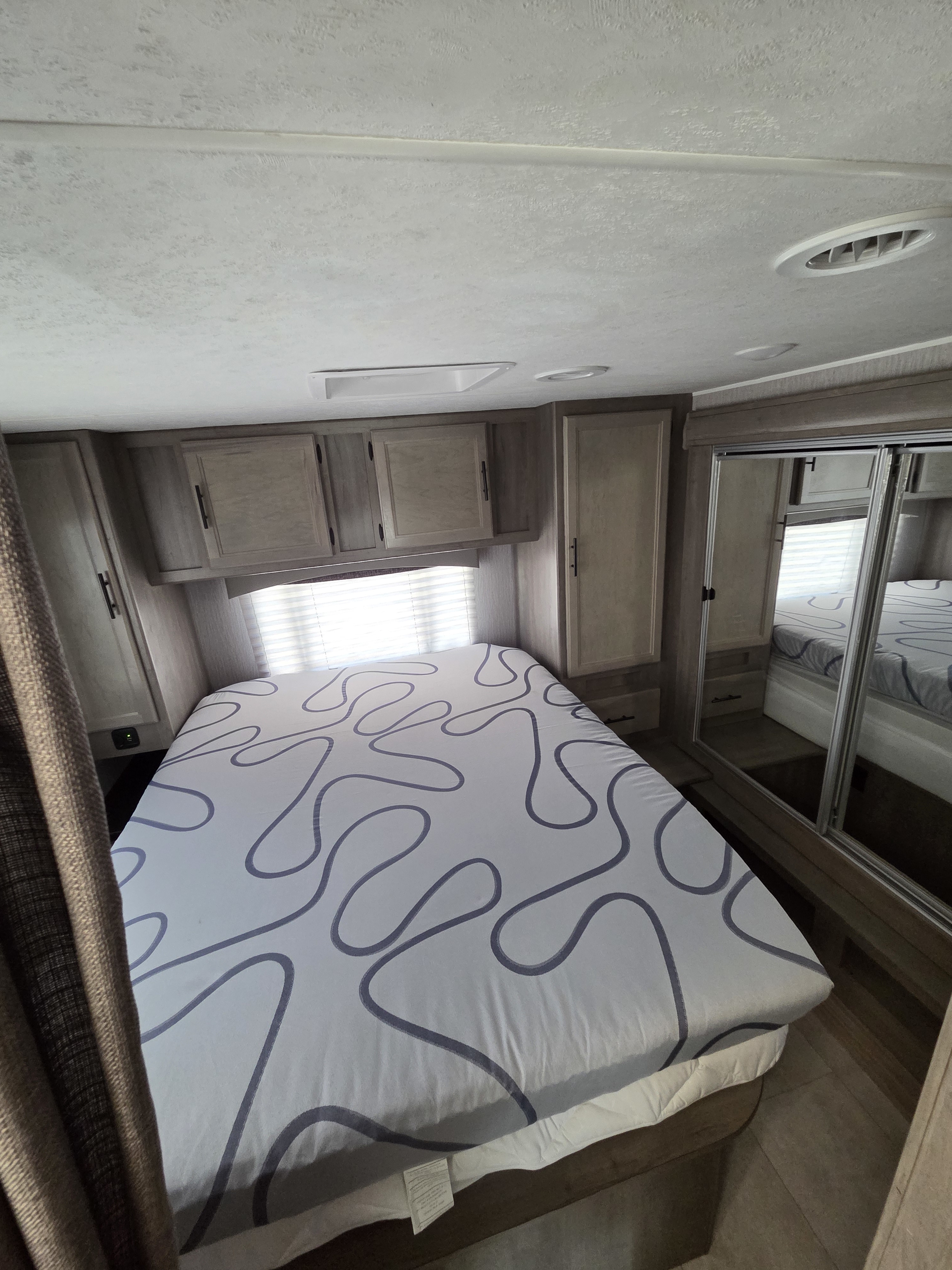 Inside this RV rental, a compact bedroom features a bed with white and gray wavy sheets, light wood cabinets, and mirrored closet.. Forest River Coachmen Freelander Premier 2022