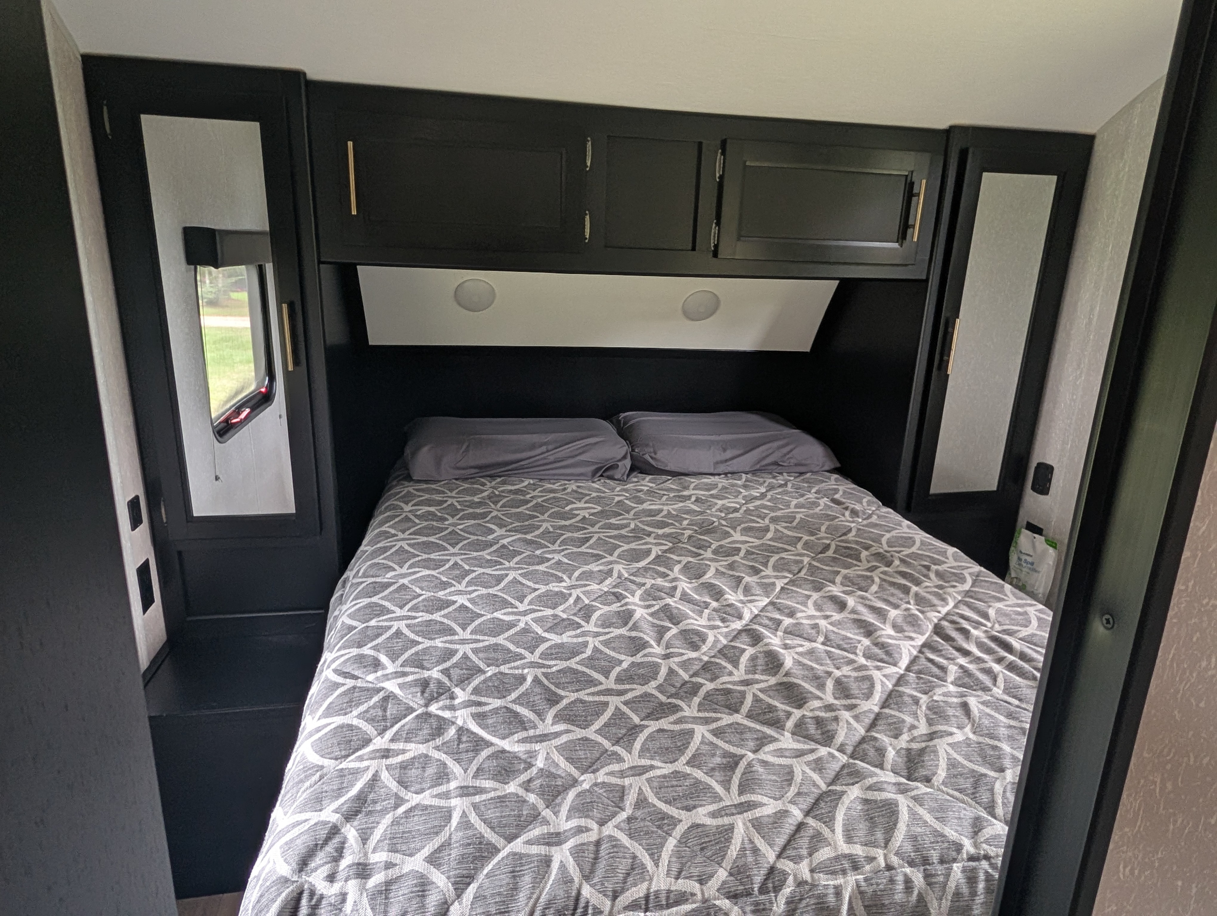 Experience compact comfort in this RV rental's bedroom, featuring dark cabinets, a patterned bed, and essential amenities.. Forest River Cherokee Grey Wolf 2021