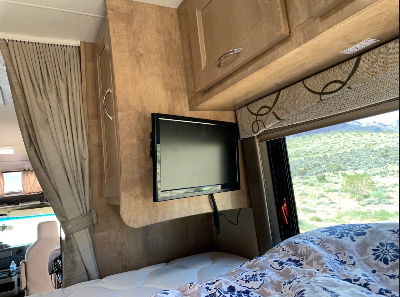 RV rental bedroom featuring a bed, TV, and a large window framing picturesque desert mountains. Ideal for travel.. Other LEPRECHAUN 220QB 2020