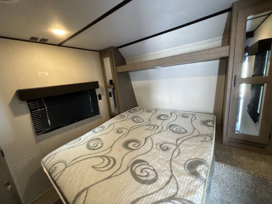 This RV rental features a comfortable bedroom with a patterned mattress, window blinds, and built-in storage.. Keystone RV Hideout LHS 2020