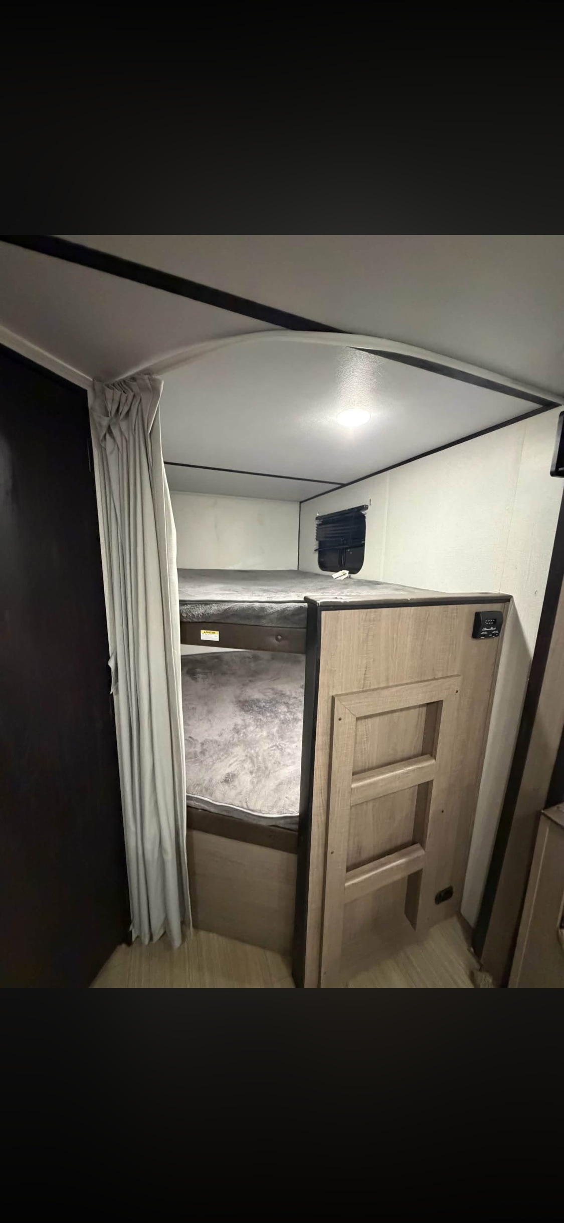 Cozy RV rental bunk beds with a ladder, privacy curtain, window, and overhead light for comfortable travel.. Keystone RV Hideout LHS 2020