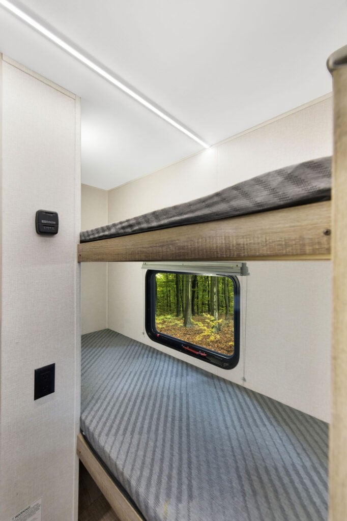 Comfortable RV rental bunk beds with a window view of a serene forest, perfect for family camping adventures.. Heartland RVs Eddie Bauer 2025