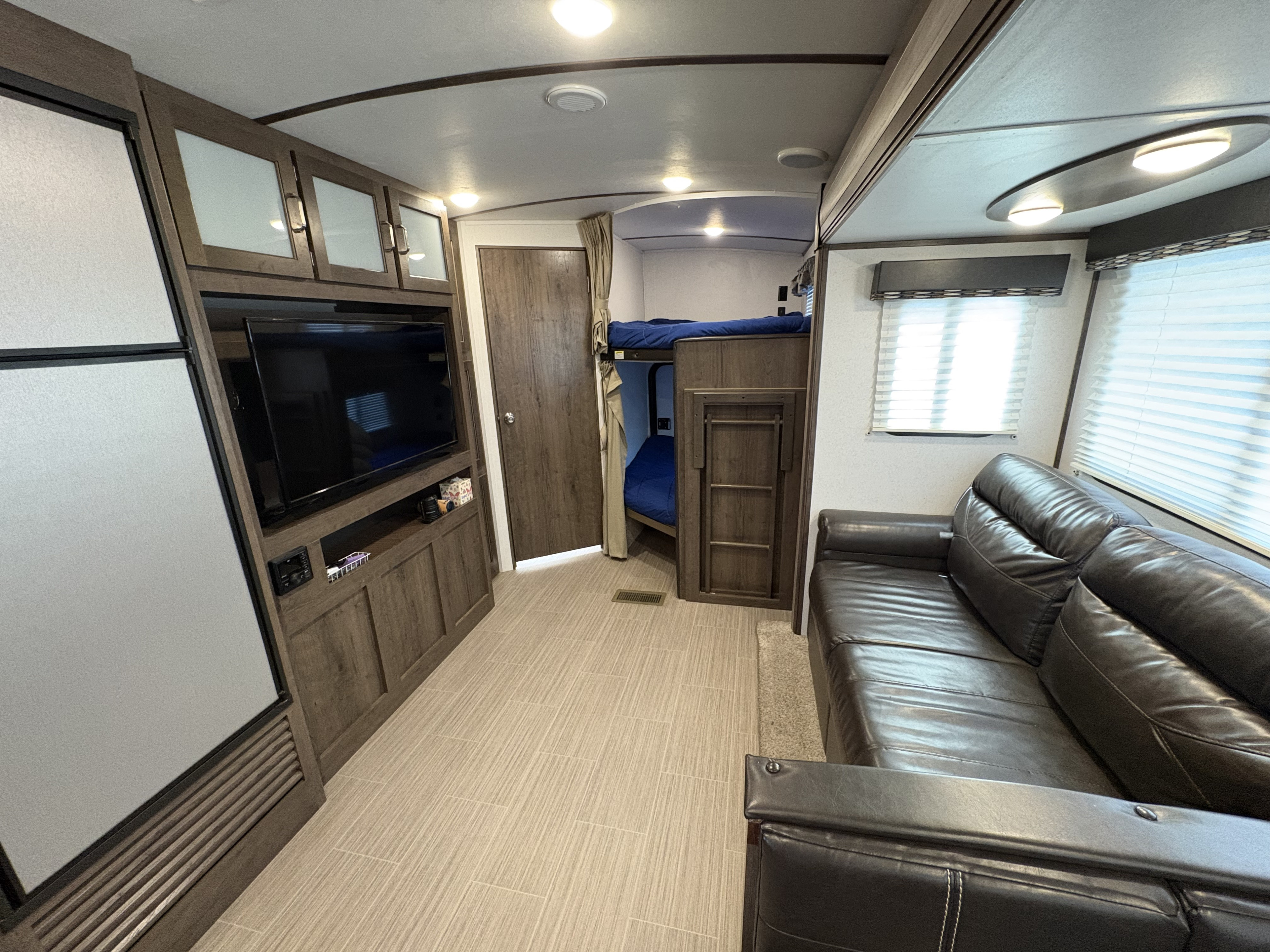 Modern RV rental interior with a living area, dark leather sofa, entertainment center, refrigerator, and bunk beds.. Keystone RV Passport Grand Touring 2020
