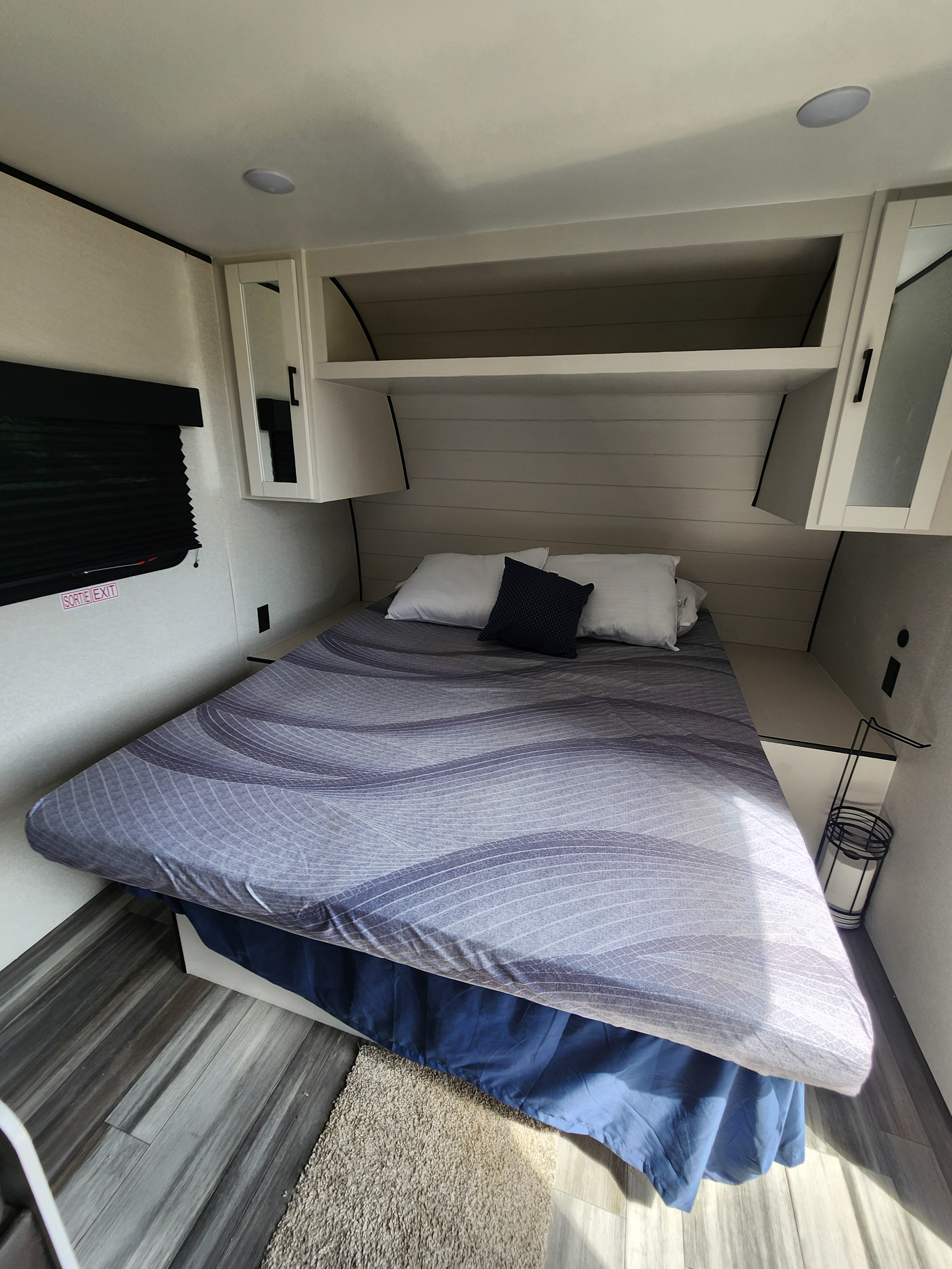 Cozy RV rental bedroom with patterned bed, overhead storage cabinets, and a prominent 'SORTIE EXIT' sign by the window.. Jayco Jay Flight SLX Sport Edition 2026