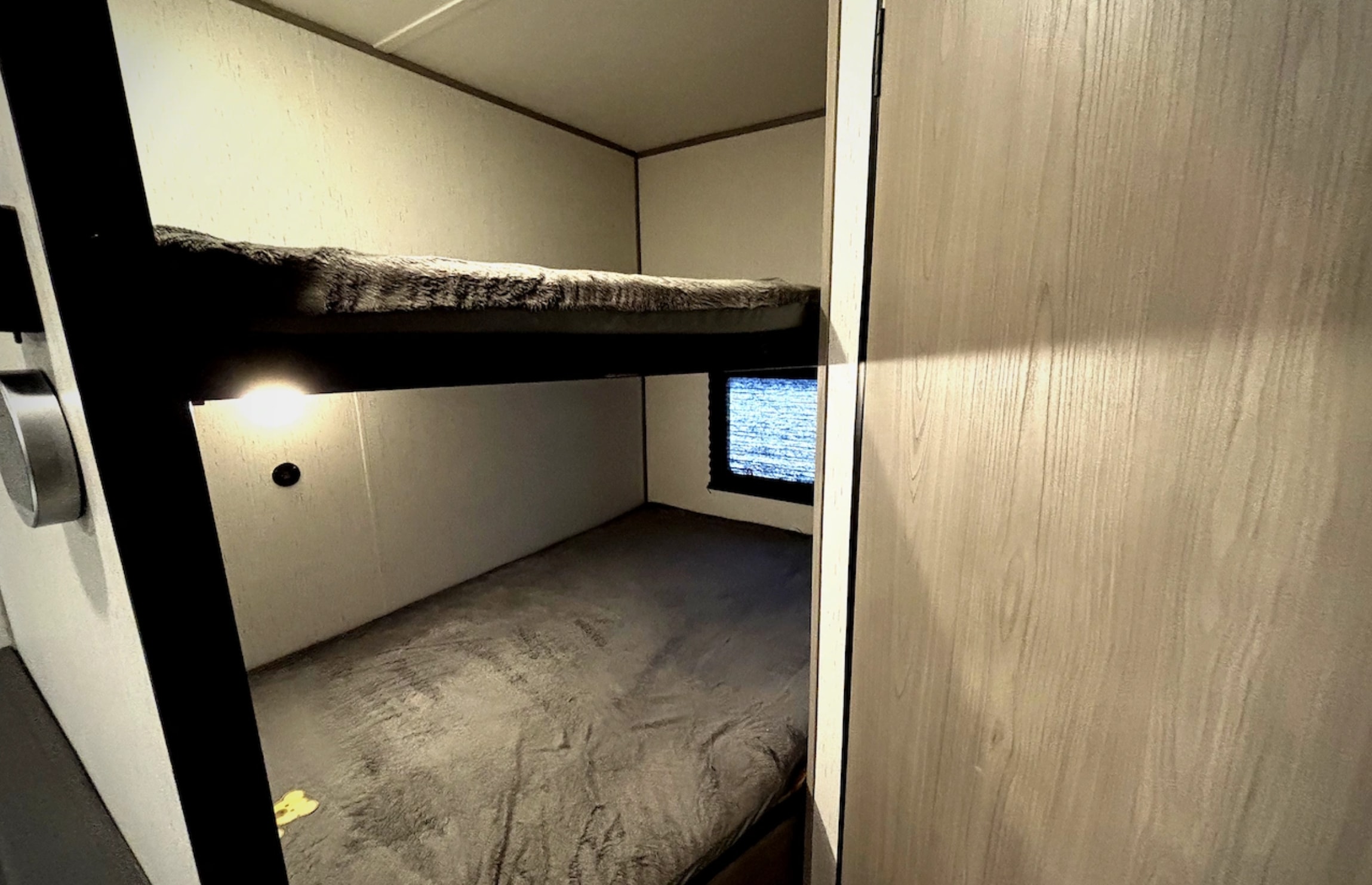 Inside an RV rental: two compact bunk beds with blankets, a small window, and a reading light. Ideal for family trips.. Dutchmen Coleman Lantern LT 2024