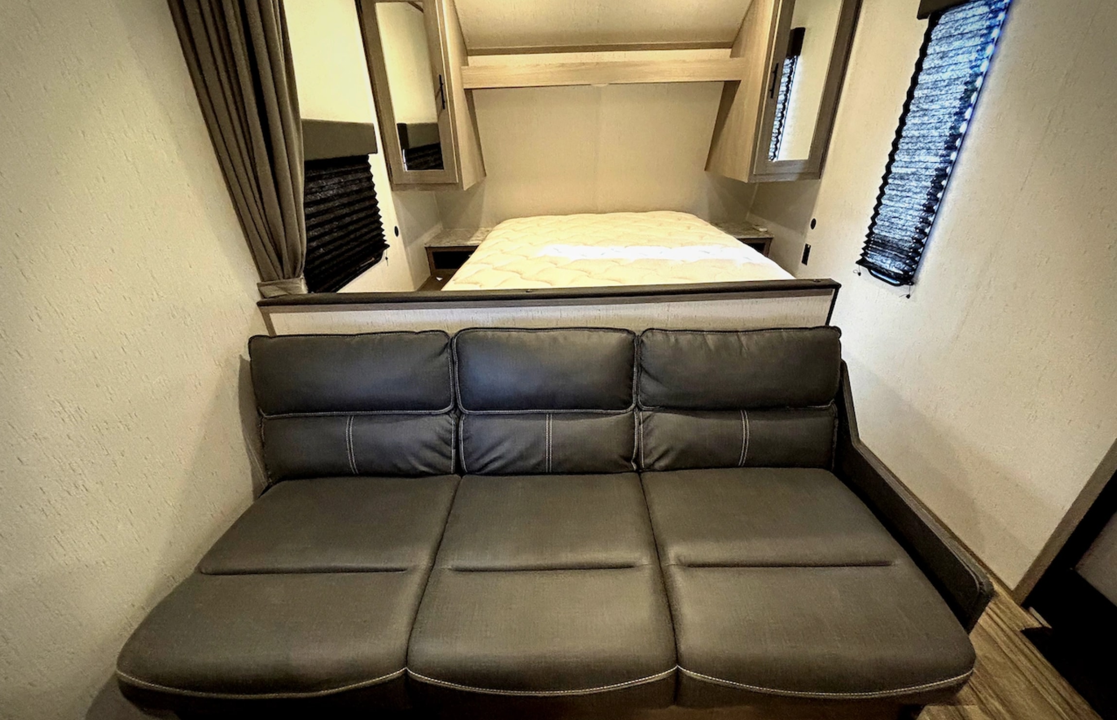 Comfortable dark gray sofa in this RV rental's compact living area, with a bed and cabinets beyond.. Dutchmen Coleman Lantern LT 2024