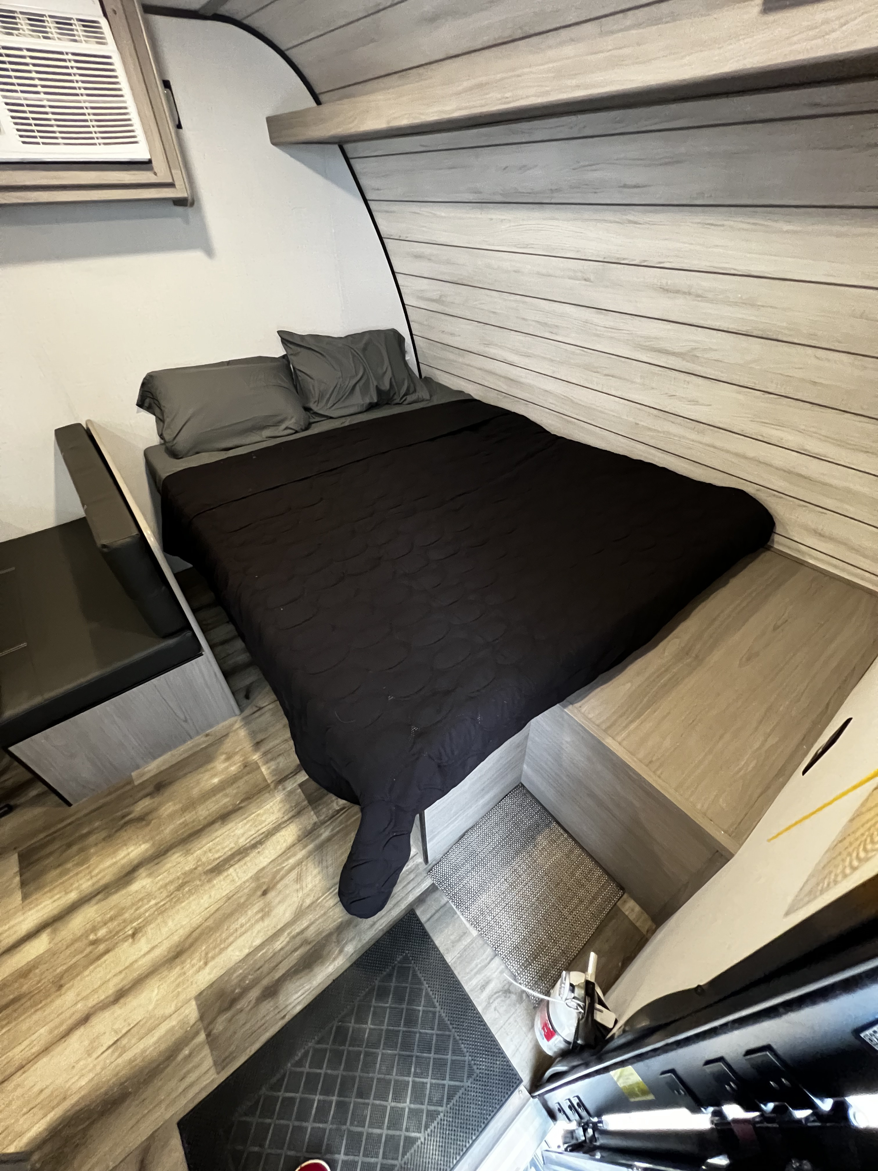 This cozy rv rental bedroom features a dark bed, gray pillows, an AC unit, wood-look walls, and integrated storage.. Dutchmen Coleman 2024