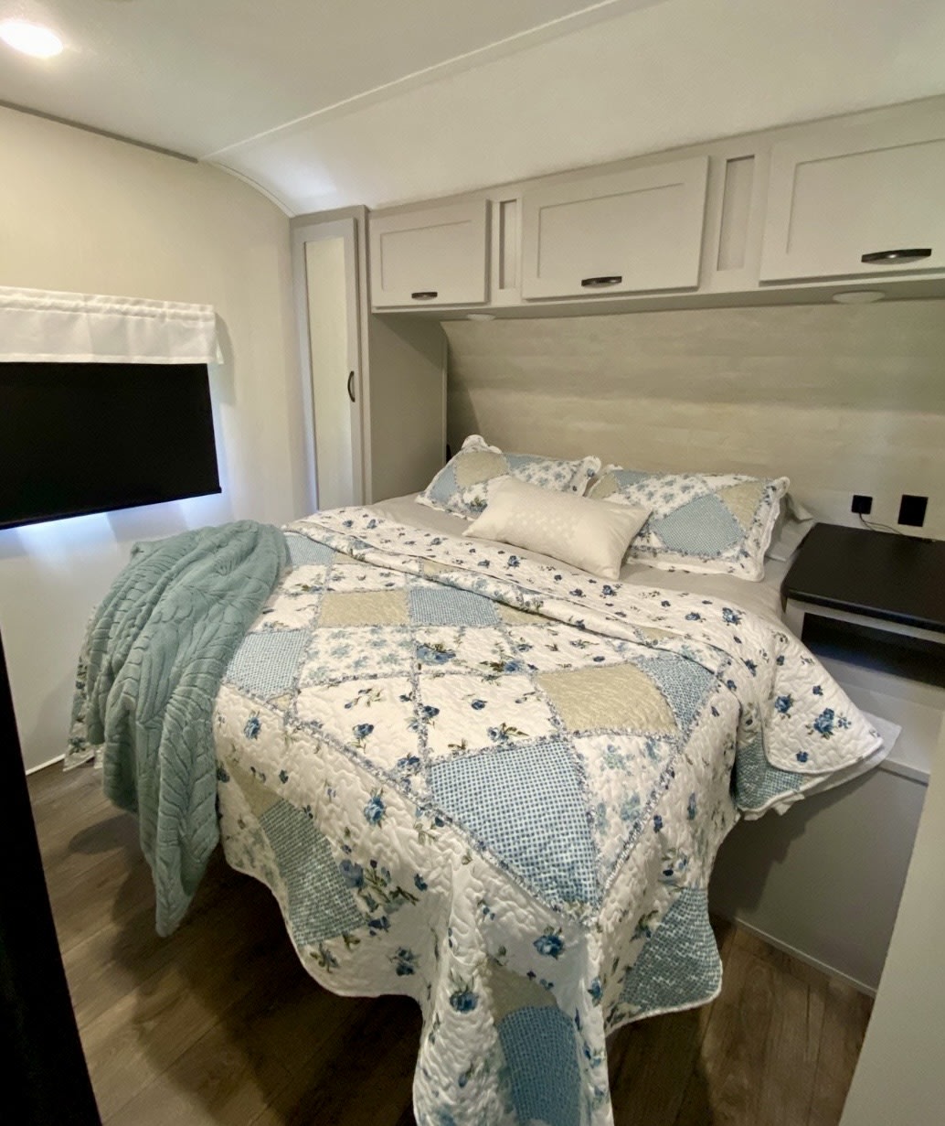Cozy RV rental bedroom featuring a blue & white patterned quilt, overhead cabinets, and a wall-mounted TV for comfort.. Forest River Vibe 2021