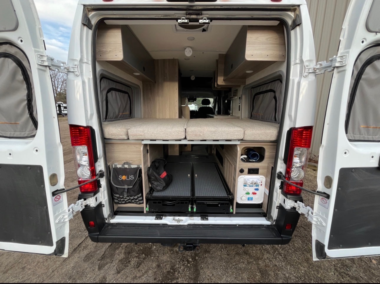 Rear view of a spacious RV rental camper van interior with comfy bed, ample under-bed storage, and pull-out trays.. Winnebago Solis-National Park Model 2023