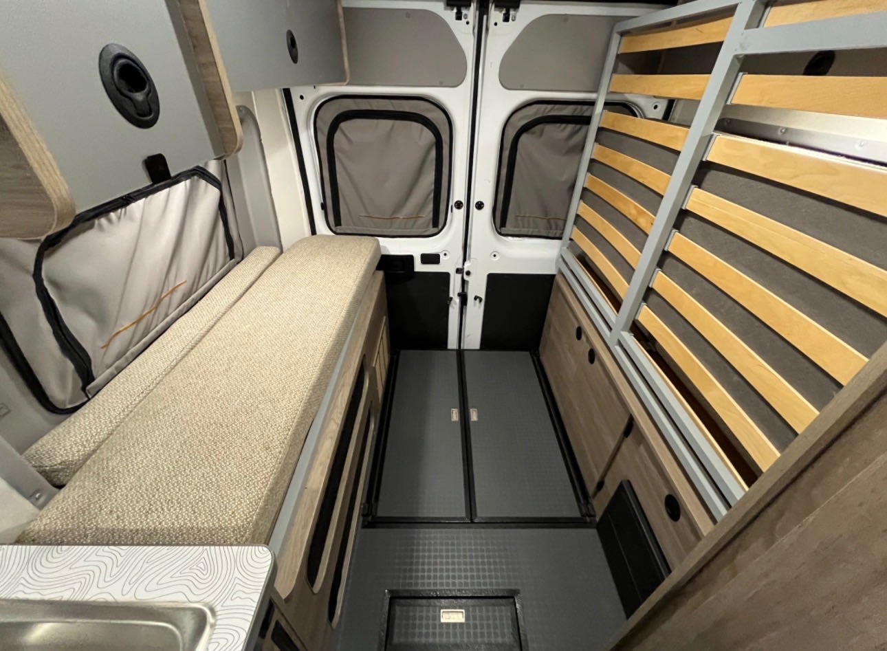 RV rental: Camper van interior with an elevated slat bed frame, cushioned bench, and storage cabinetry. Dark floor, ready for adventure.. Winnebago Solis-National Park Model 2023