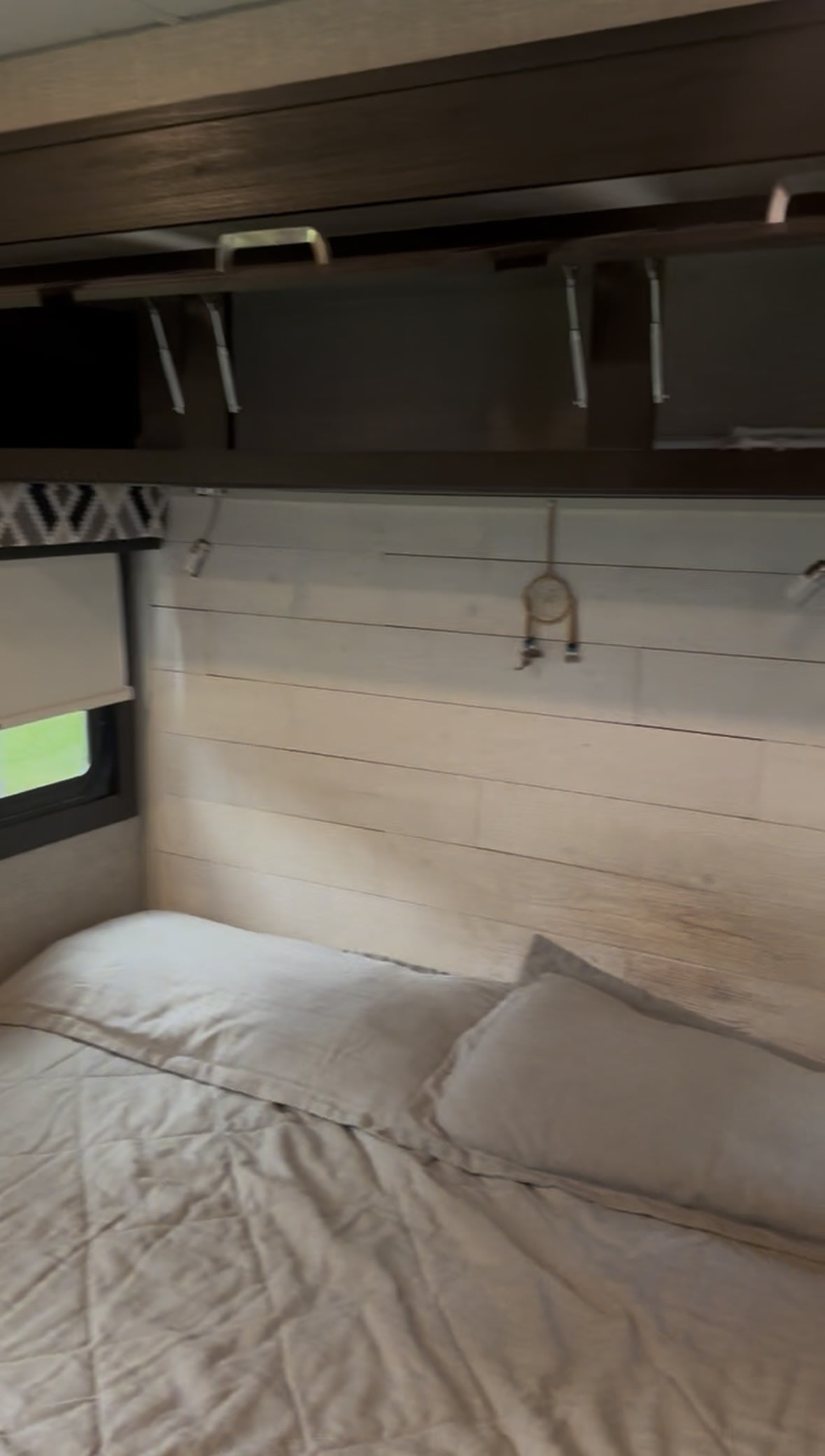 Cozy RV rental bedroom featuring a comfortable bed with light bedding, overhead storage cabinets, and a window with a green view.. Jayco Precept 2022