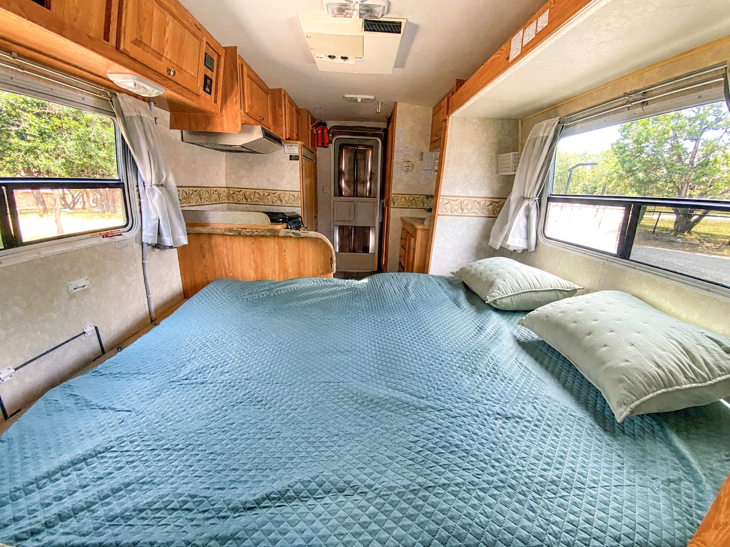 Cozy RV rental interior showcasing a spacious bed, functional kitchen, and scenic window views for camping.. R-Vision Trail-Lite 2002