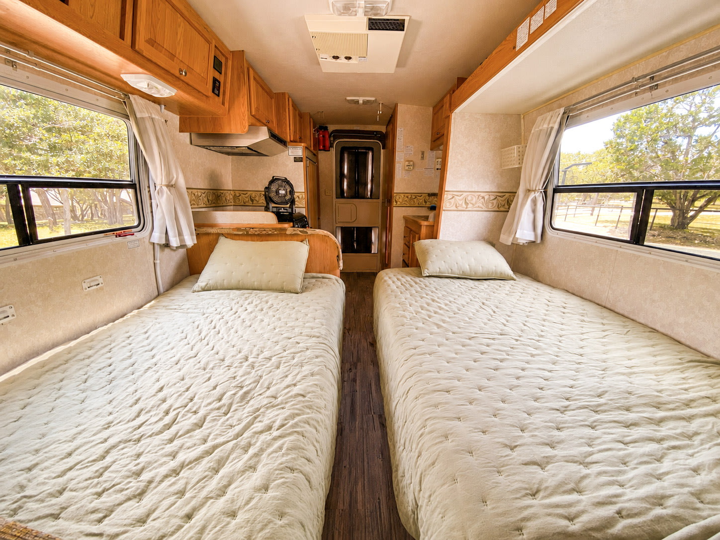 Cozy twin beds in an RV rental, with light quilted bedding, windows, and wooden cabinetry for travelers.. R-Vision Trail-Lite 2002