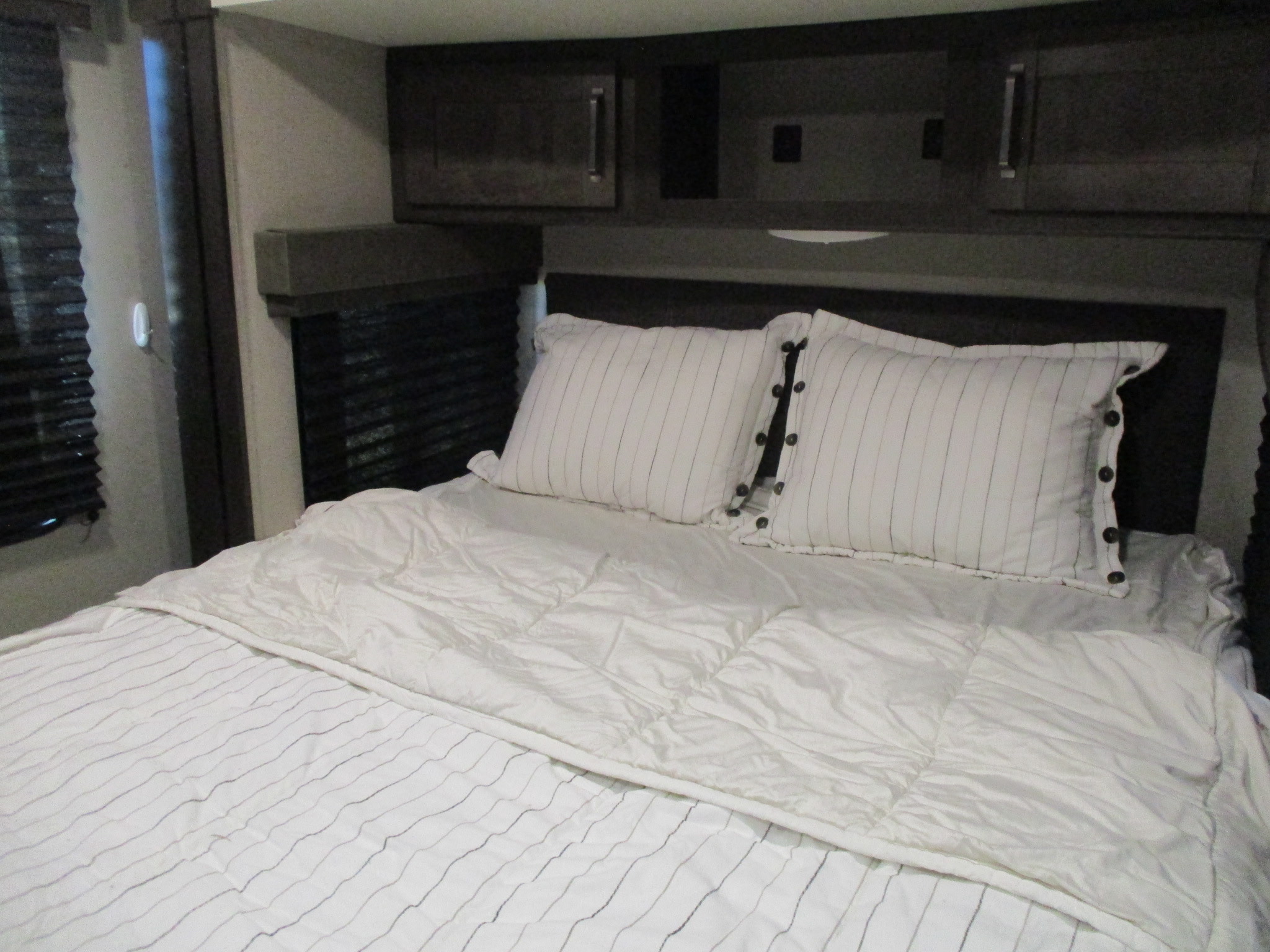Well-made bed in a cozy RV rental bedroom. White bedding, striped pillows, and overhead storage for comfortable travel.. Grand Design Transcend Xplor 2022