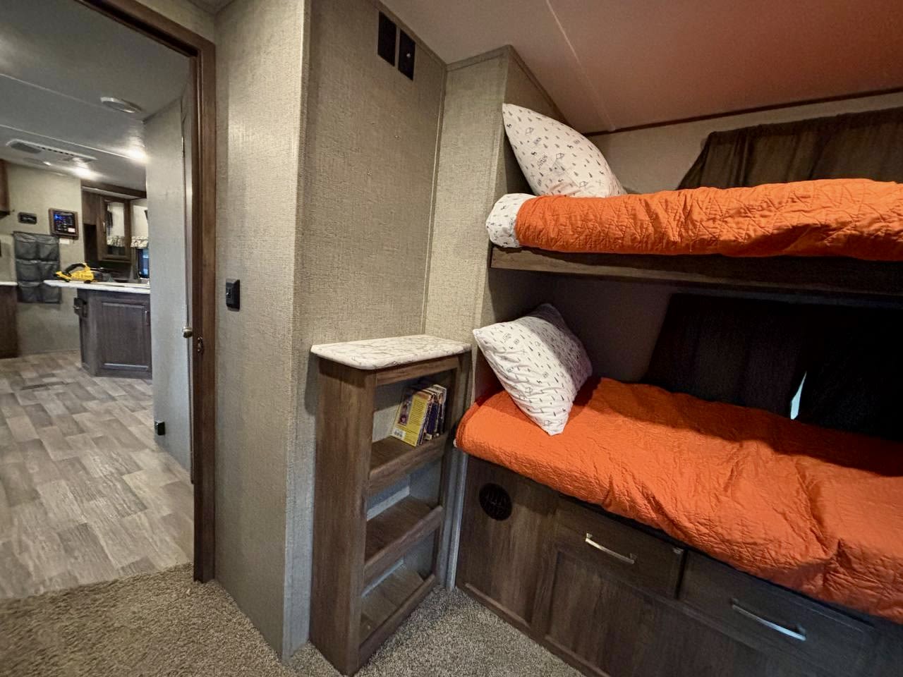 Cozy RV rental bunk beds with orange bedding and storage, looking into the kitchen/living area with wood floors.. Keystone RV Cougar 2018