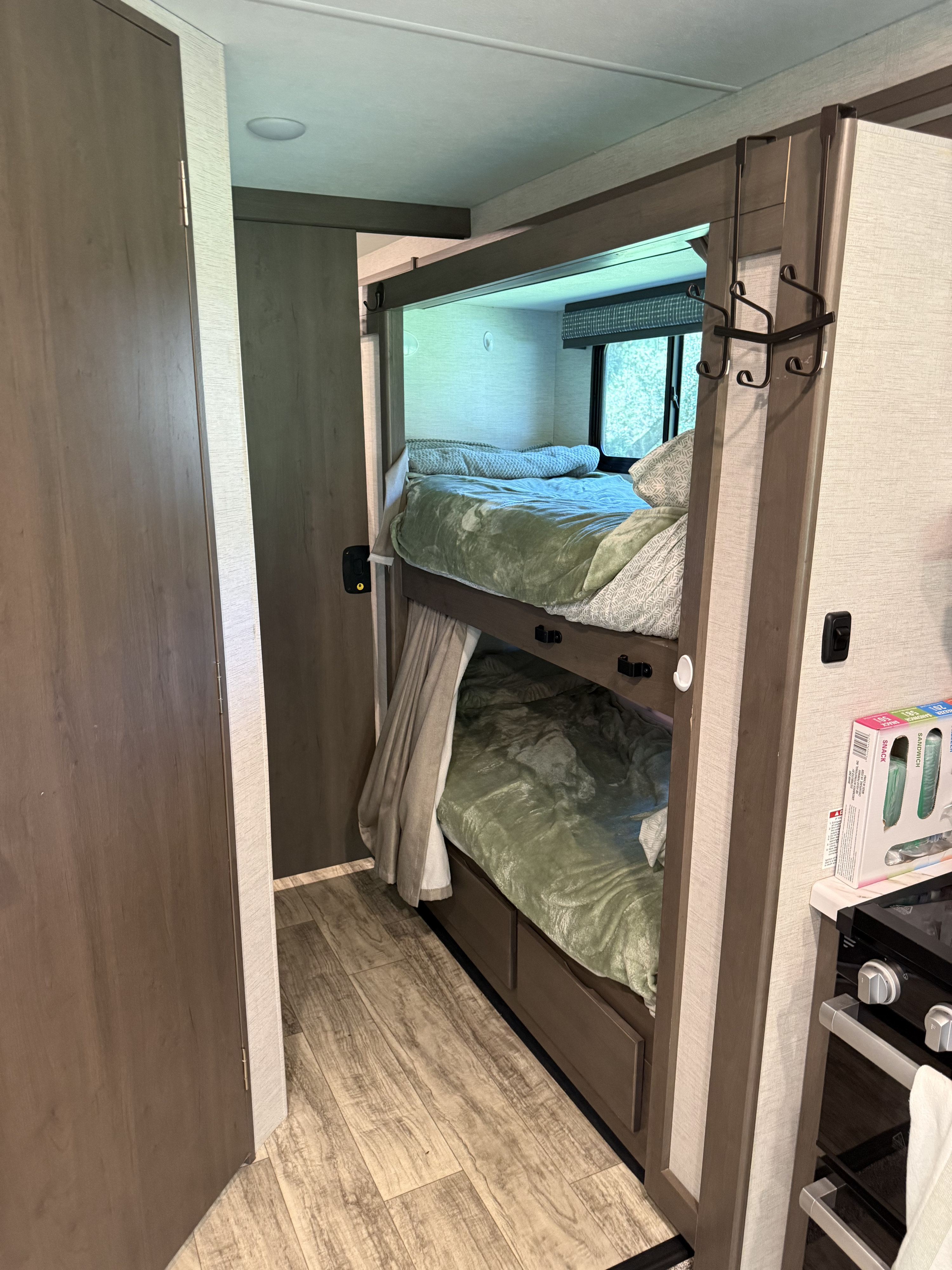 RV rental: Compact bunk beds with light green bedding, a window, an adjacent door, and a glimpse of the kitchen area.. Thor Chateau 2025