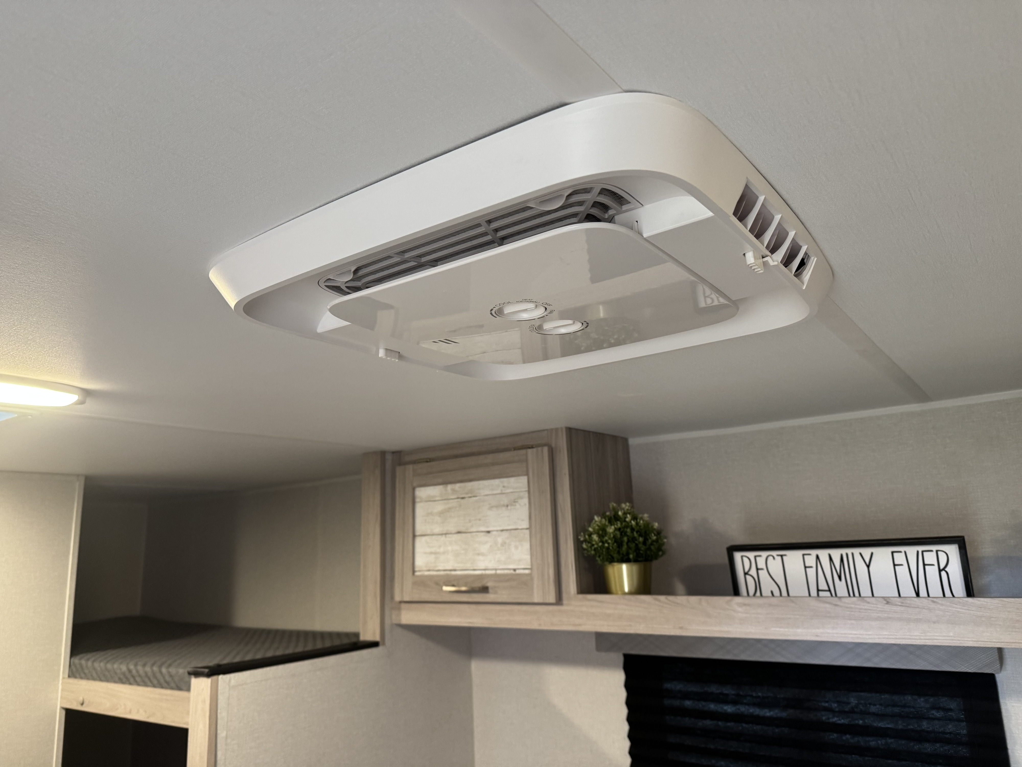 RV rental interior featuring a ceiling AC unit, bunk bed, cabinets, and a decorative "BEST FAMILY EVER" sign.. Heartland RVs Pioneer 2025