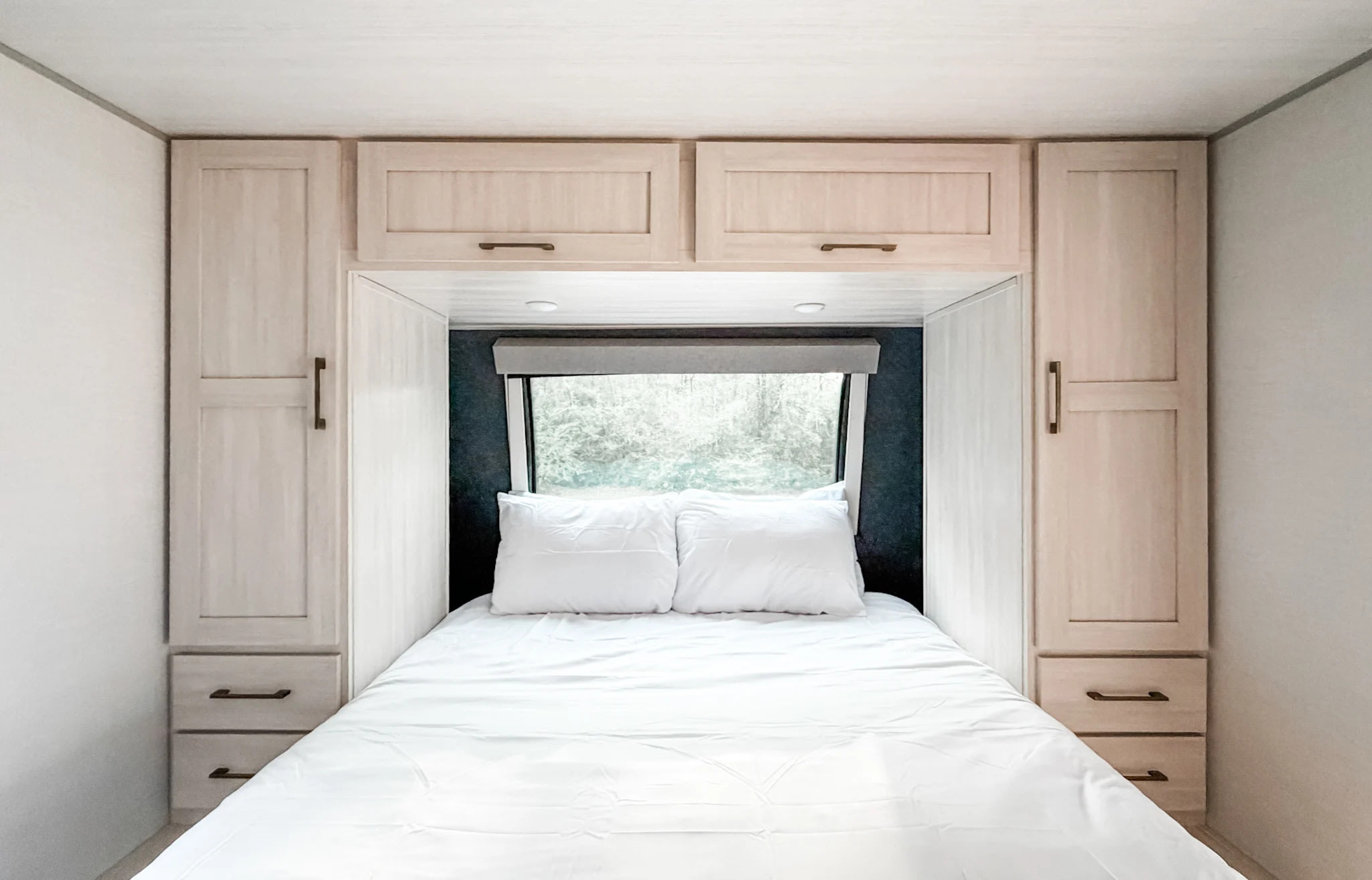 Cozy RV rental bedroom with a white bed, wood cabinetry, and a window revealing a blurred nature view. Ideal for relaxation.. Forest River Surveyor Legend 2026