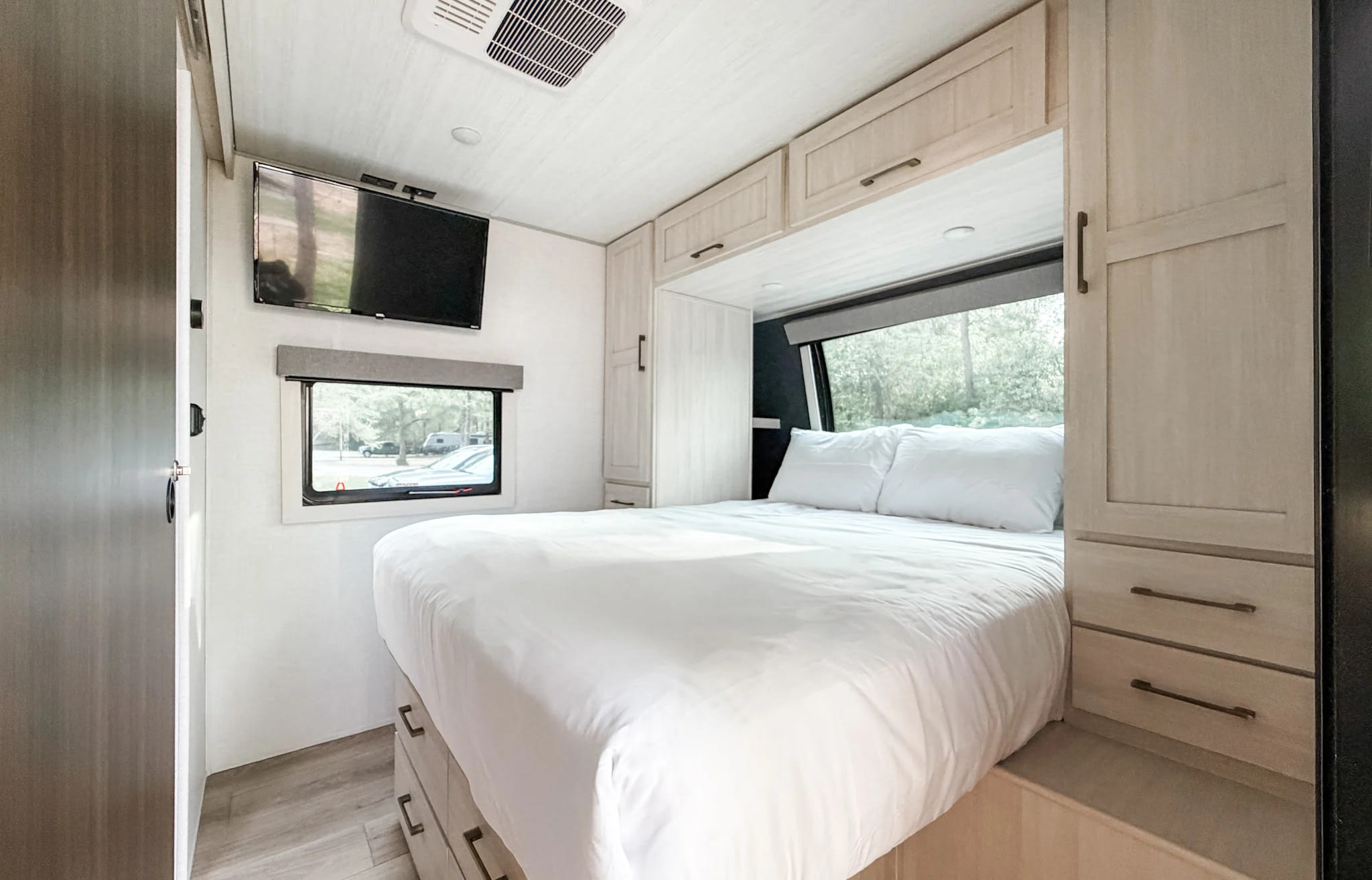 Bright RV rental bedroom showcasing a comfortable white bed, TV, window view, and light wood storage.. Forest River Surveyor Legend 2026
