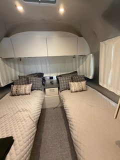Inside this RV rental, find a tidy bedroom with twin beds, quilted bedspreads, overhead cabinets, and a central nightstand.. Airstream Flying Cloud 2025