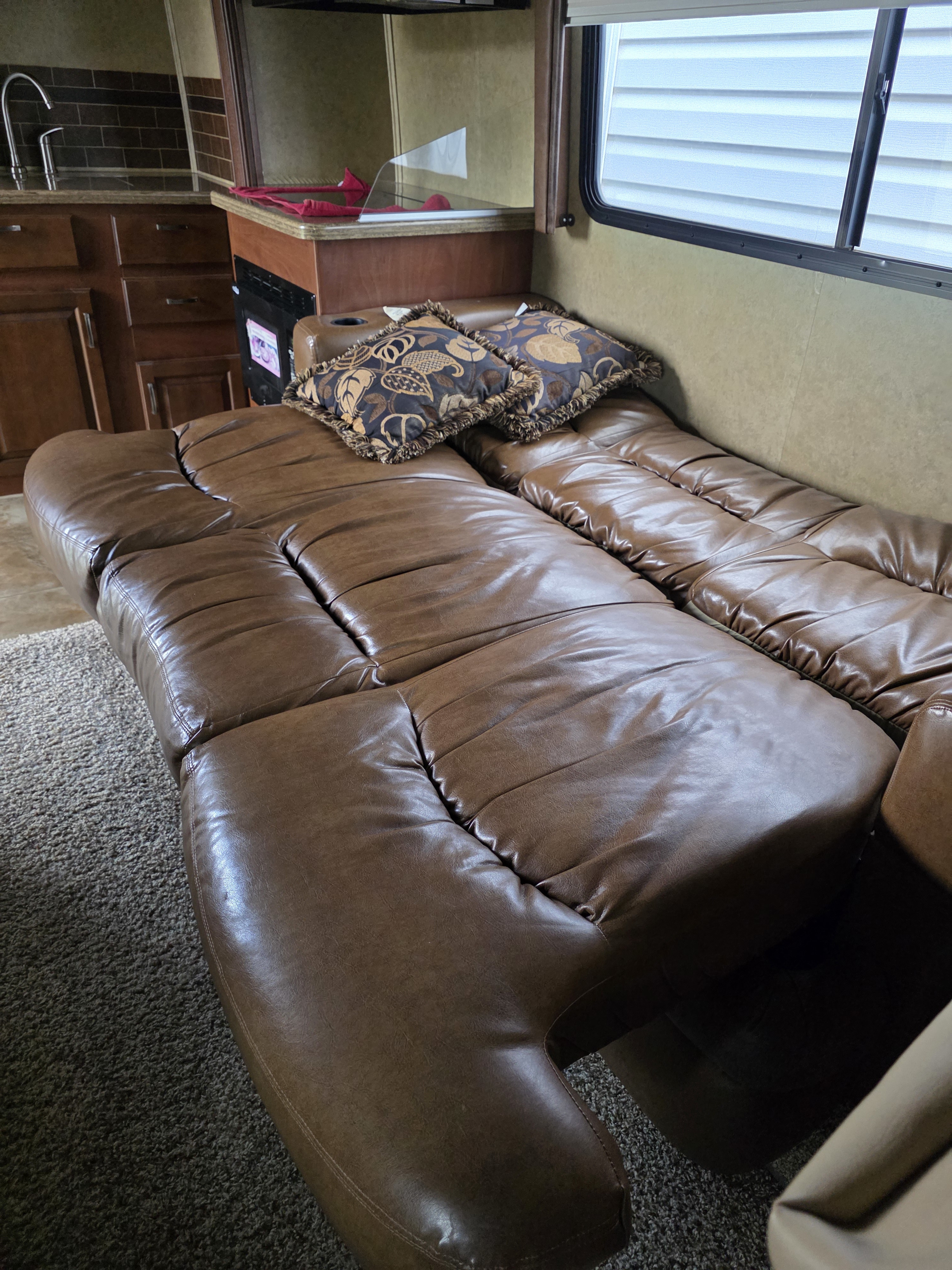 Comfortable brown leather RV rental interior with a reclining sofa, decorative pillows, and a compact kitchen area.. Jayco Melbourne 2013