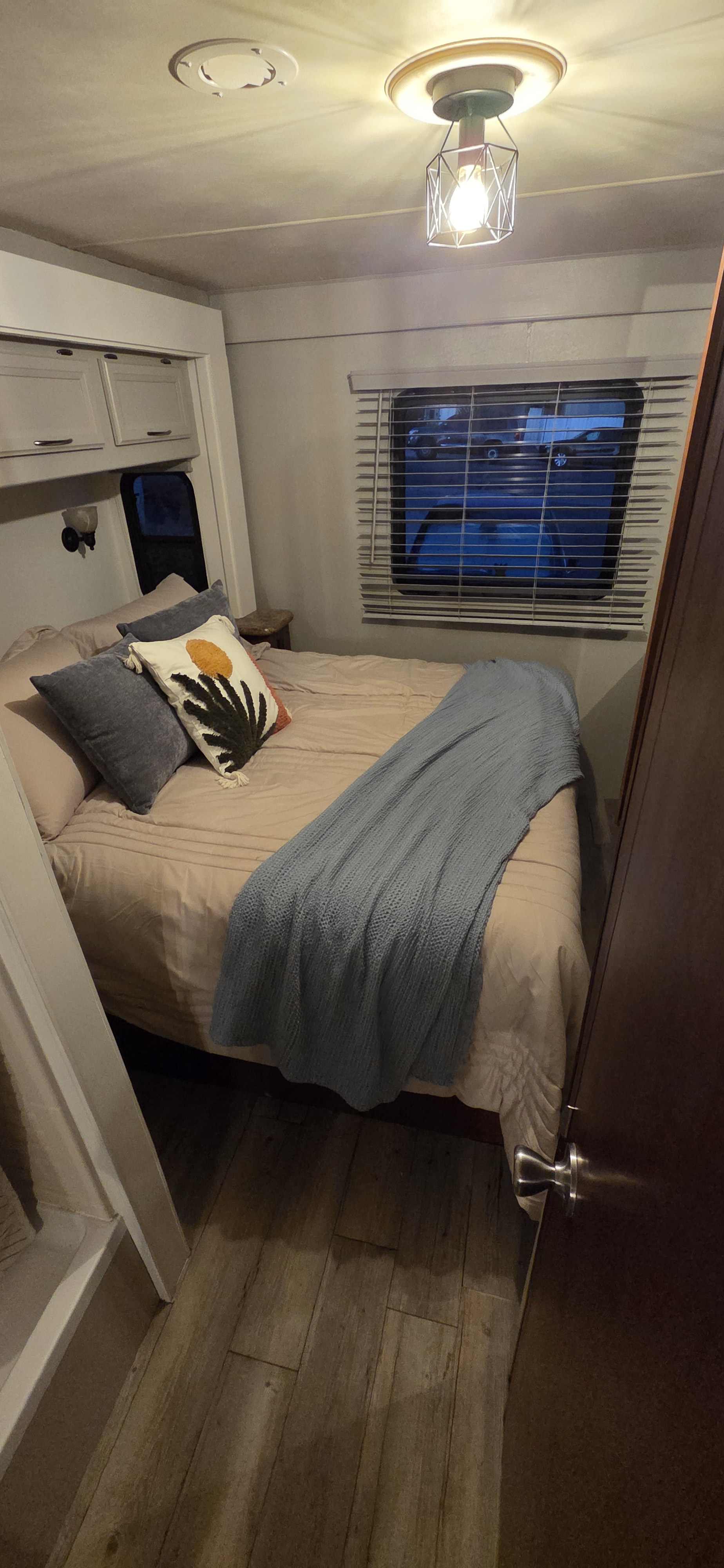 RV rental bedroom with a bed, light bedding, blue throw blanket, decorative pillow, window with blinds, wood-look floor, and overhead lights.. Thor Freedom Elite 2014