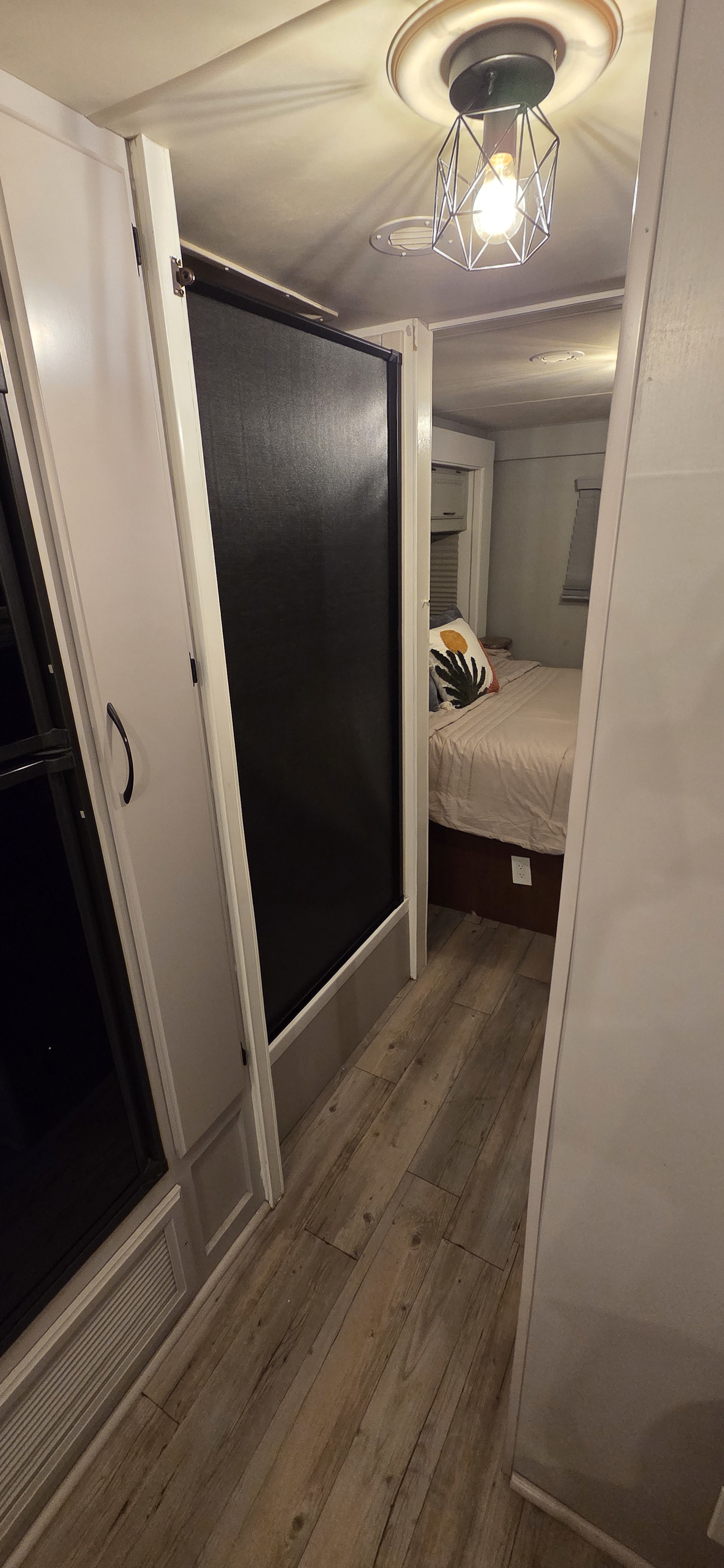 Bright RV rental interior: A hallway with wood floors leads to a cozy bedroom with light bedding, a patterned pillow, and modern ceiling light.. Thor Freedom Elite 2014