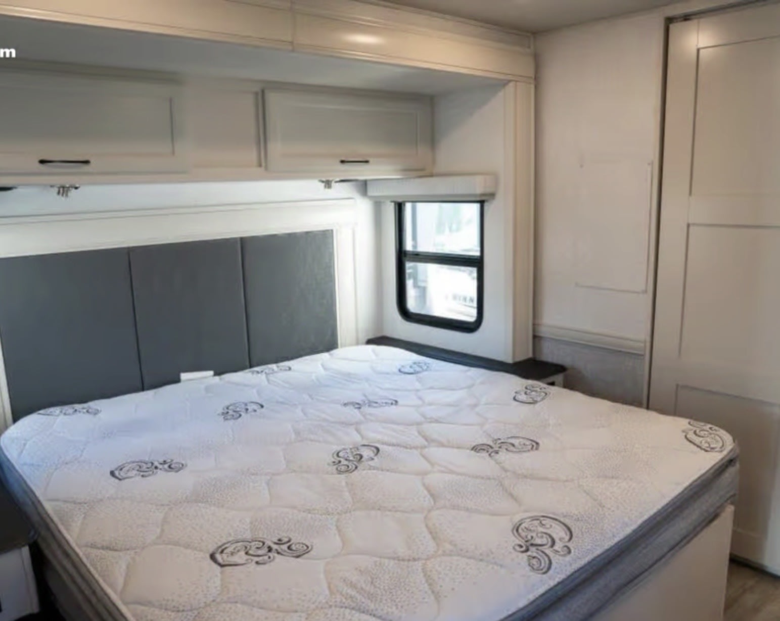 Cozy RV rental bedroom with a patterned mattress, gray padded headboard, and overhead storage cabinets.. Holiday Rambler Admiral 2024