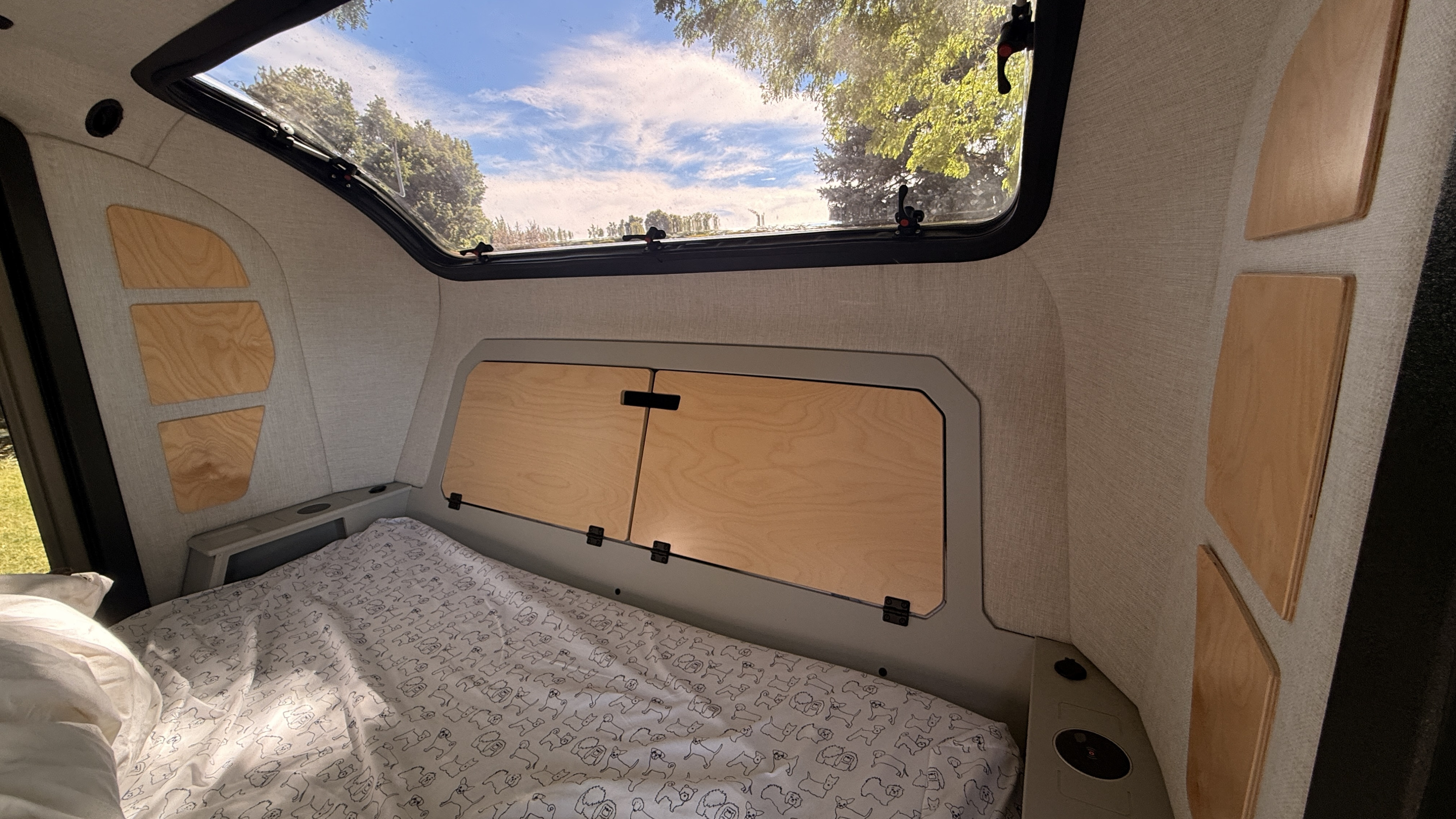 Cozy RV rental bedroom with dog-patterned sheets, wooden storage, and a large scenic window. Perfect for nature lovers!. Escapod Topo 2 2023