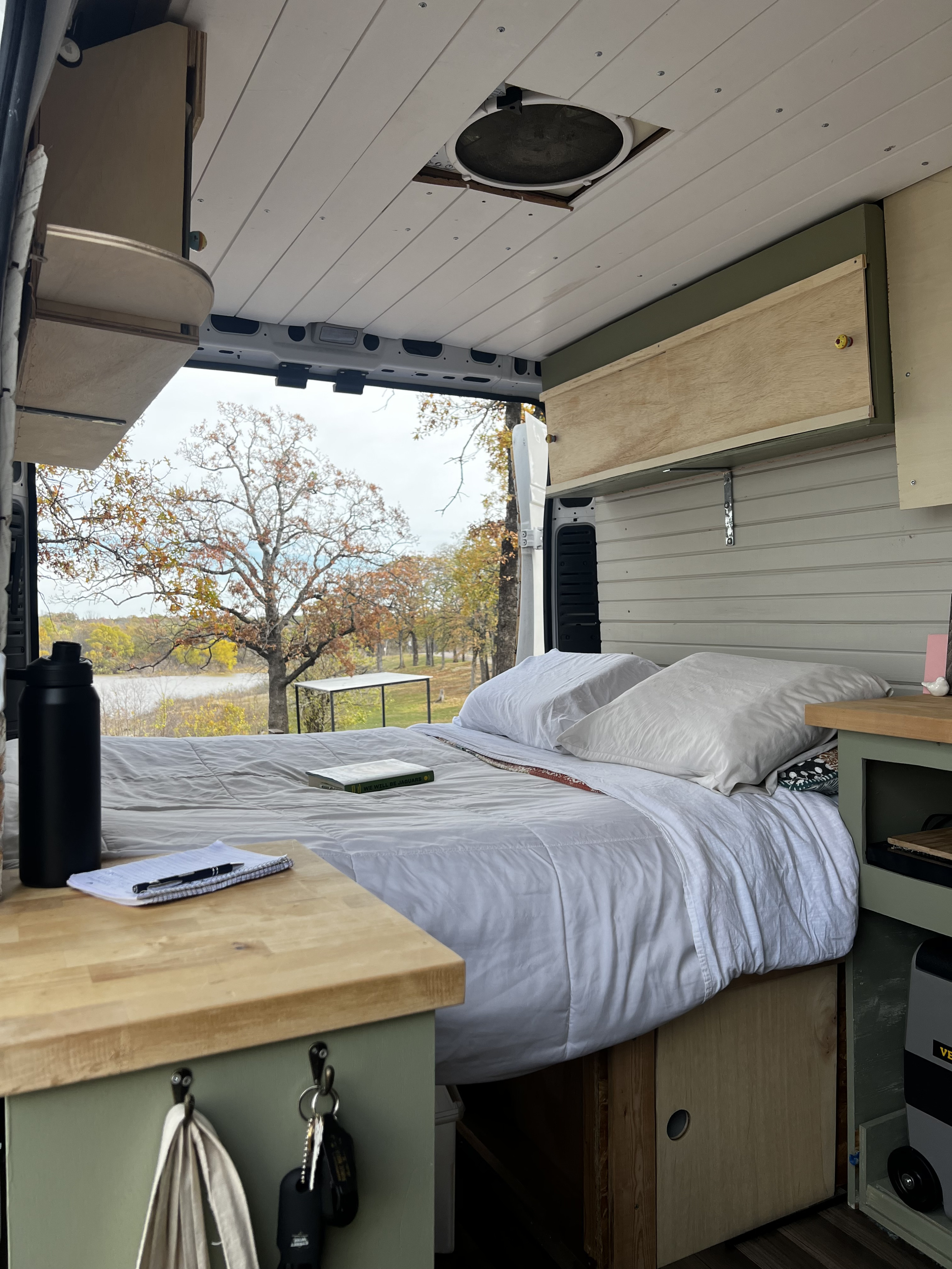 This cozy RV rental features a comfortable bed overlooking an autumn lake, with a handy workspace and storage for an ideal getaway.. Dodge Promaster 2500 high roof 2019