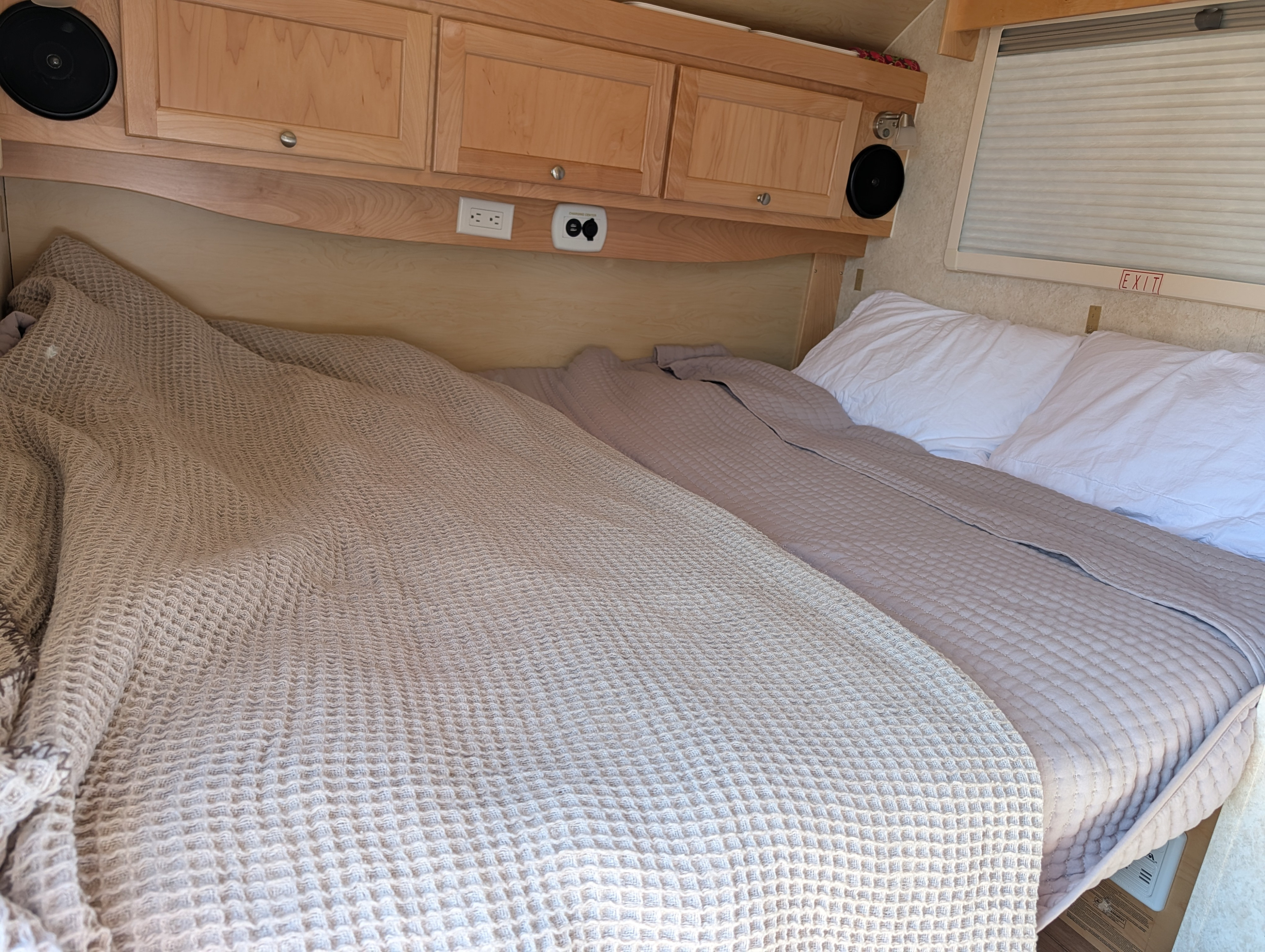 RV rental sleeping area features two cozy beds, wooden cabinets, power outlets, speakers, and a window with a blind.. nuCamp T@B CS-S 2017