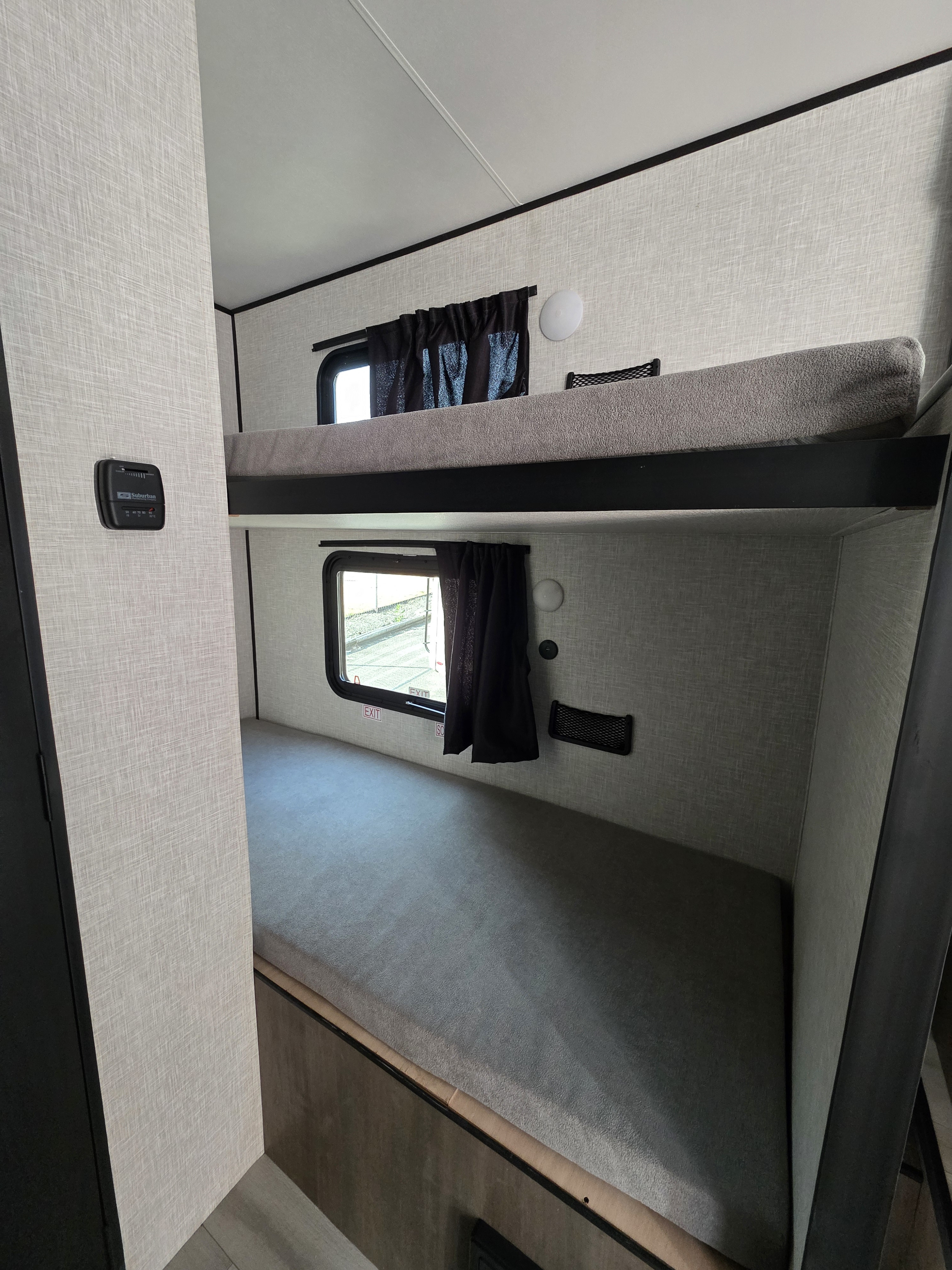 Cozy bunk bed interior of an RV rental, featuring two sleeping berths with windows, mesh storage, lights, and a thermostat.. Starcraft Autumn Ridge 2025