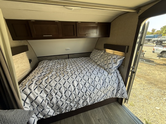 Cozy RV rental bedroom with patterned bedding, dark wood cabinets, and a view to the outside through an open door.. Forest River Cherokee Wolf Pup 2018