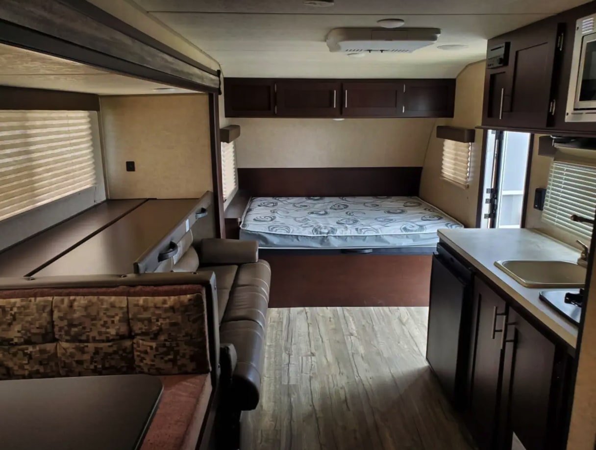 This rv rental interior features a cozy bed, compact kitchen, dining area, and bunk beds, offering ample space for travelers.. Forest River Cherokee Wolf Pup 2018