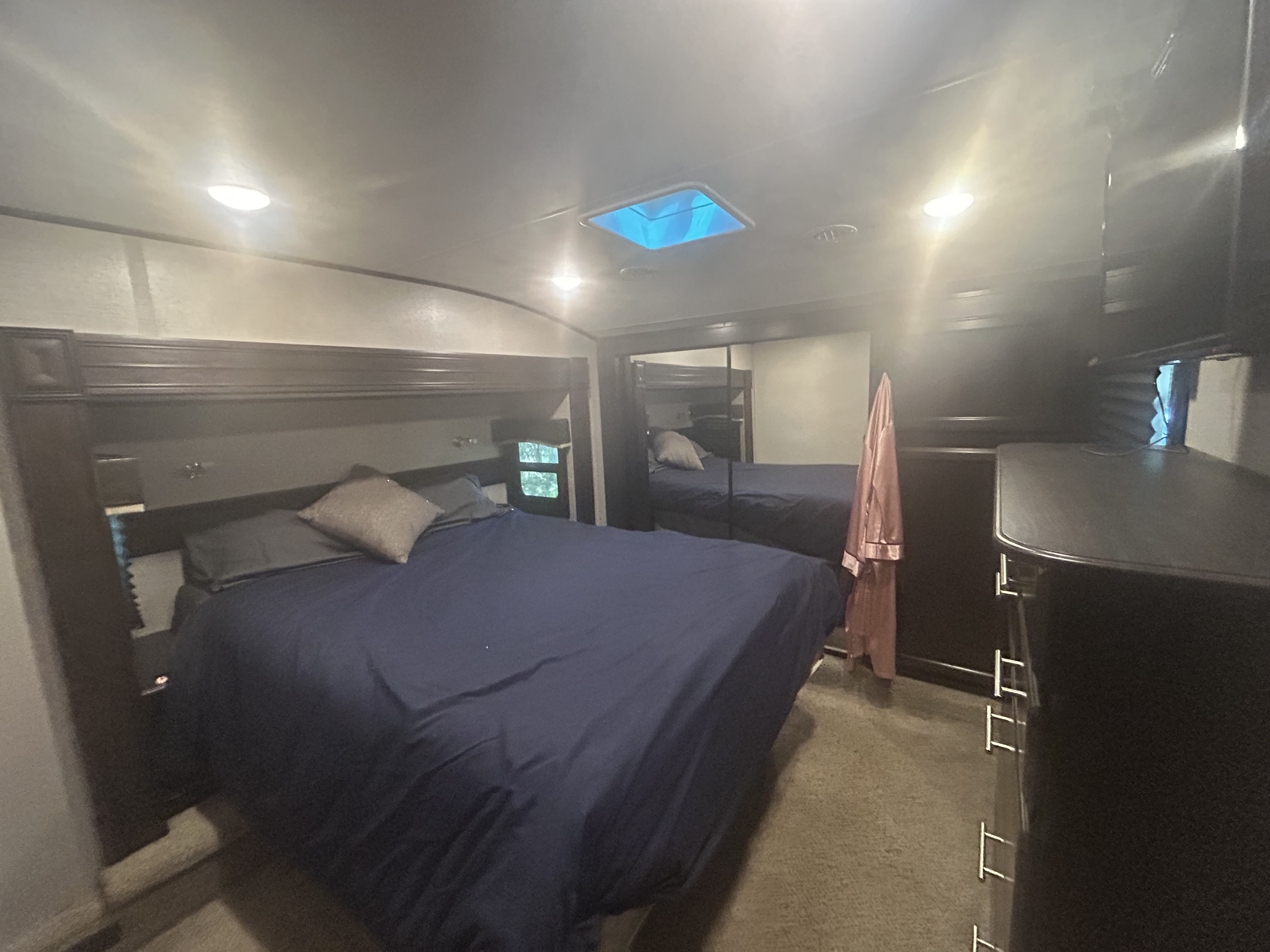 RV rental bedroom featuring a dark blue bed, mirrored closet, dresser, and ceiling lights. View of the cozy interior.. Jayco Eagle 2019