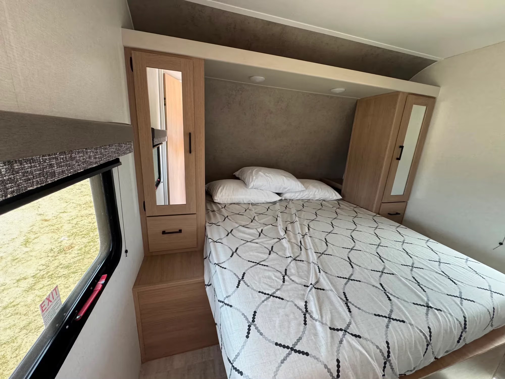 RV rental: A cozy bedroom with a patterned bed, wood cabinets, overhead lighting, and window with an emergency EXIT sign.. Aspen Trail LE 2026