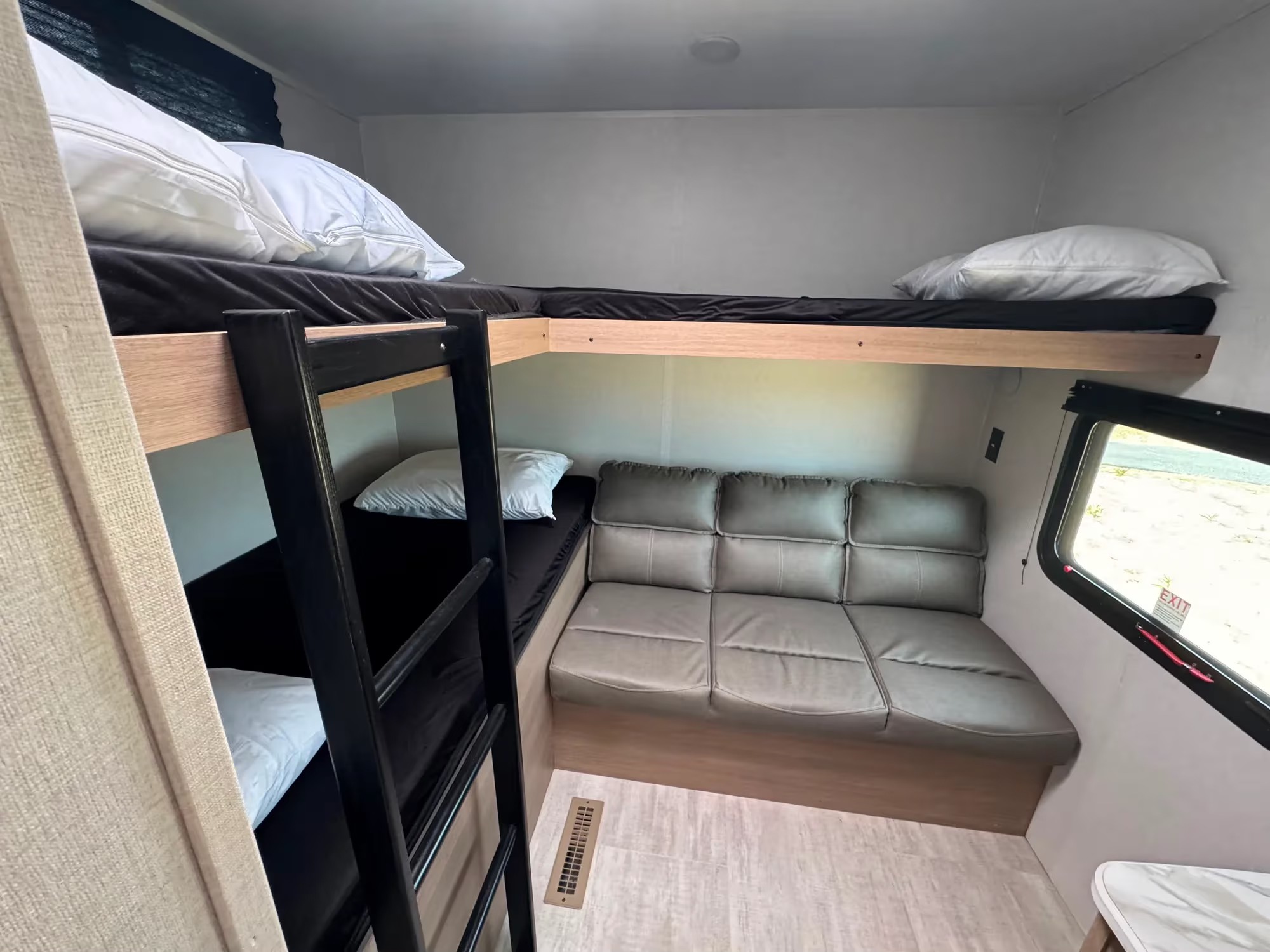 RV rental interior showing a bunk bed area, a cozy sofa, and a window. This compact setup provides sleeping and seating.. Aspen Trail LE 2026