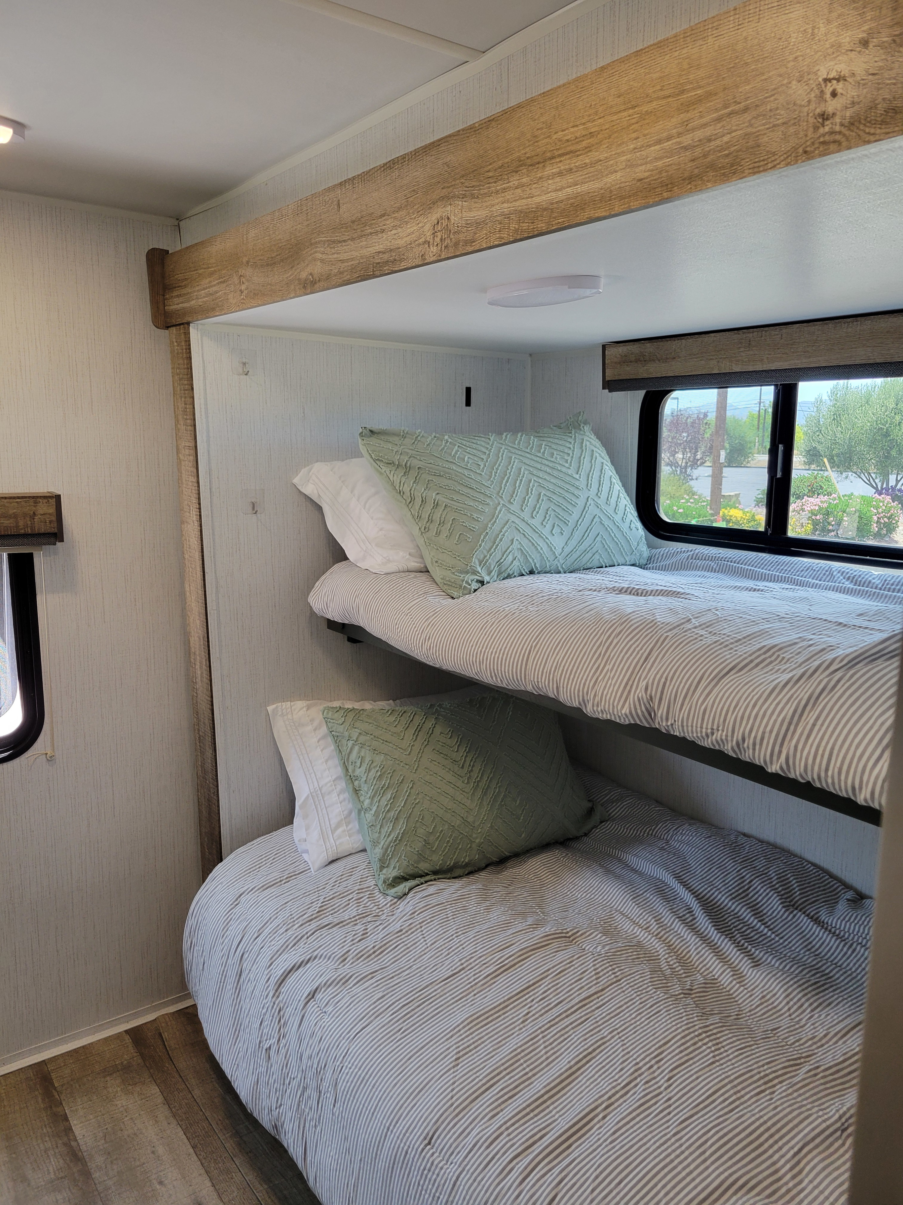 Modern rv rental interior with stacked bunk beds, featuring cozy striped bedding and soft green pillows.. Heartland RVs Eddie Bauer 2024