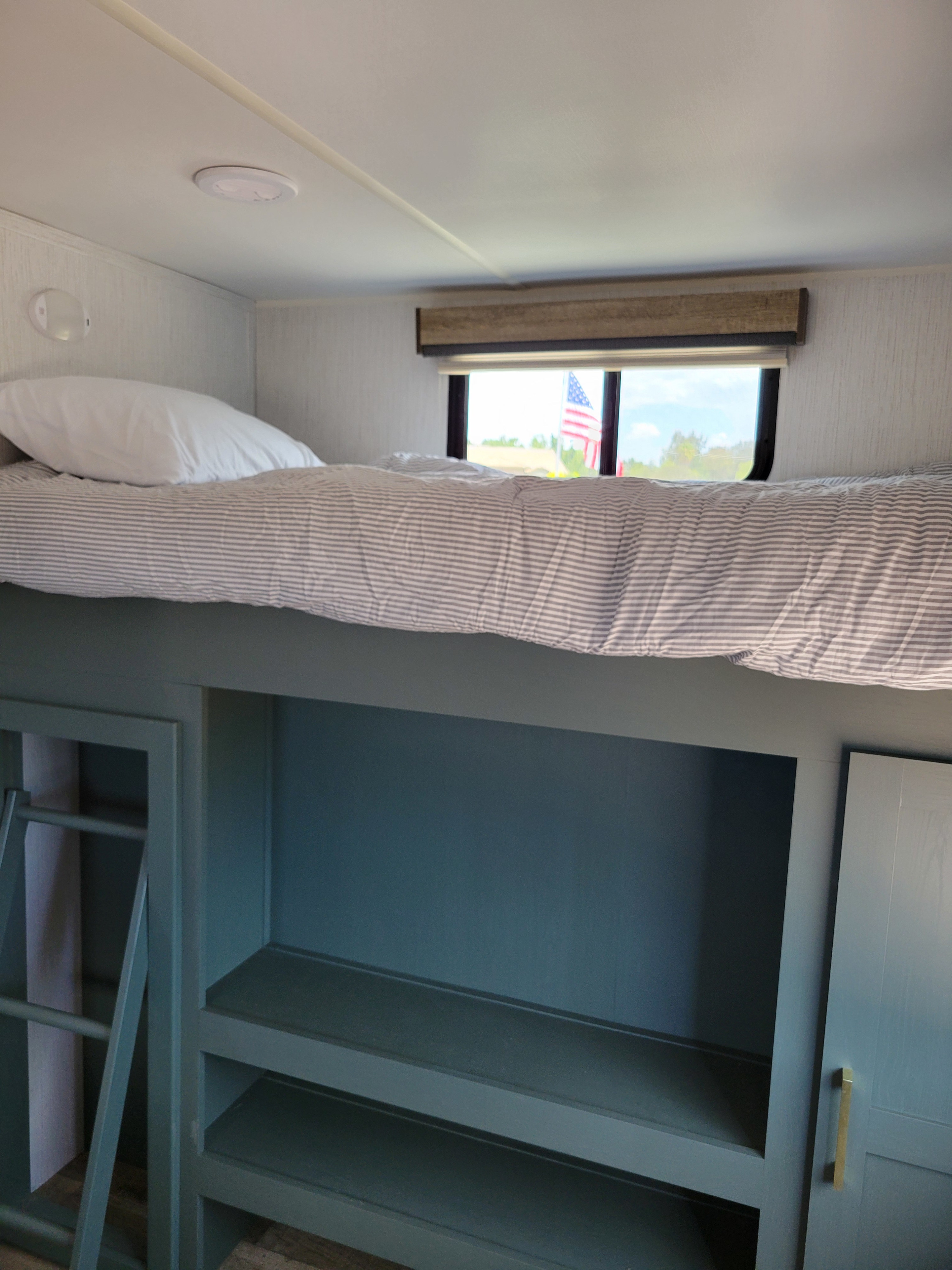 rv rental bunk area with striped bedding, shelves, and a window revealing an American flag.. Heartland RVs Eddie Bauer 2024