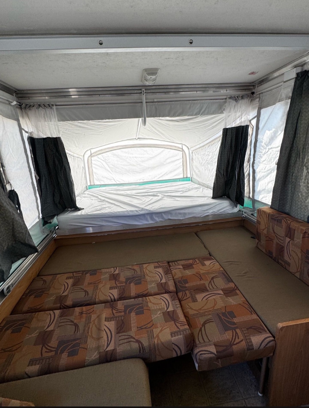 Enjoy this pop-up RV rental interior with a bed, curtains, and convertible seating. Perfect for your next camping trip!. Fleetwood Discovery 2007
