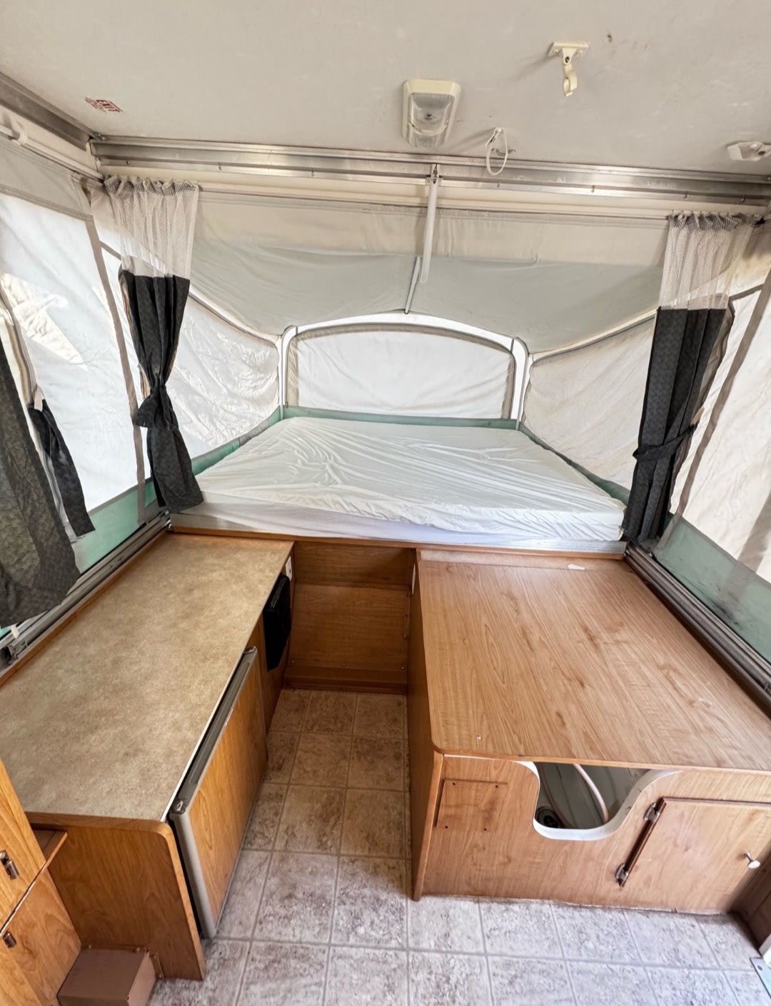 This pop-up camper rv rental interior features a large bed, wood cabinetry, and a light-colored tiled floor.. Fleetwood Discovery 2007
