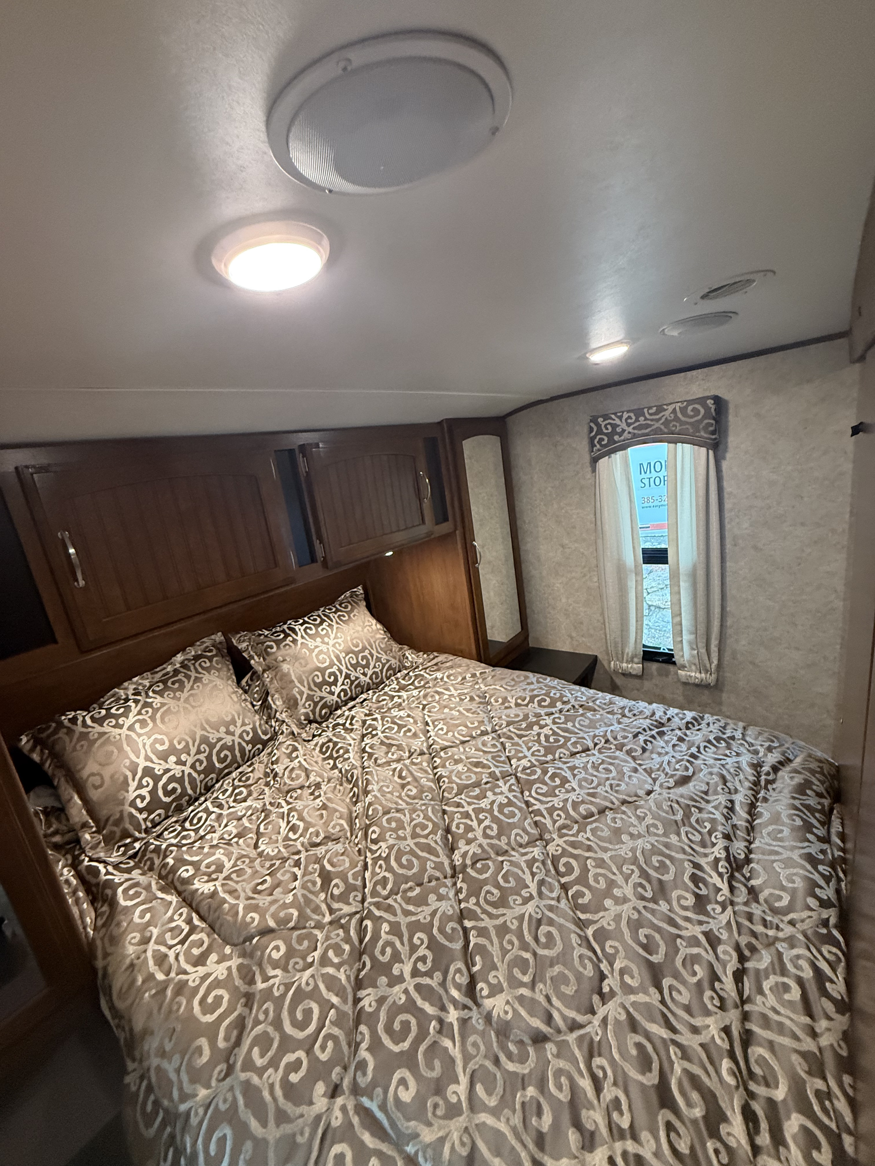 Cozy RV rental bedroom featuring a patterned comforter, overhead storage, and a small window for a comfortable stay.. Jayco White Hawk 2017