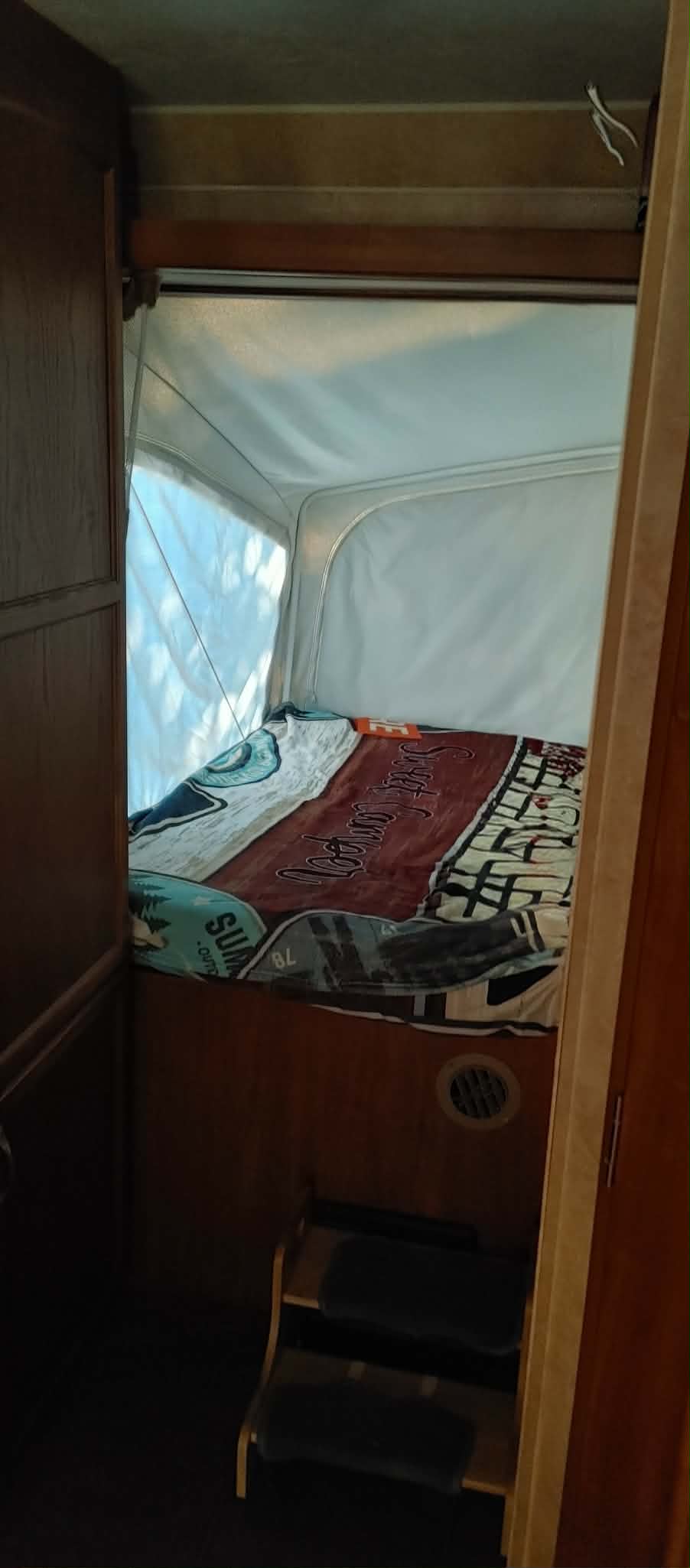 View into an rv rental pop-out bed, featuring a cozy bed with patterned blankets, steps, and soft-sided walls.. Jayco Jay Feather Select EXP 2011