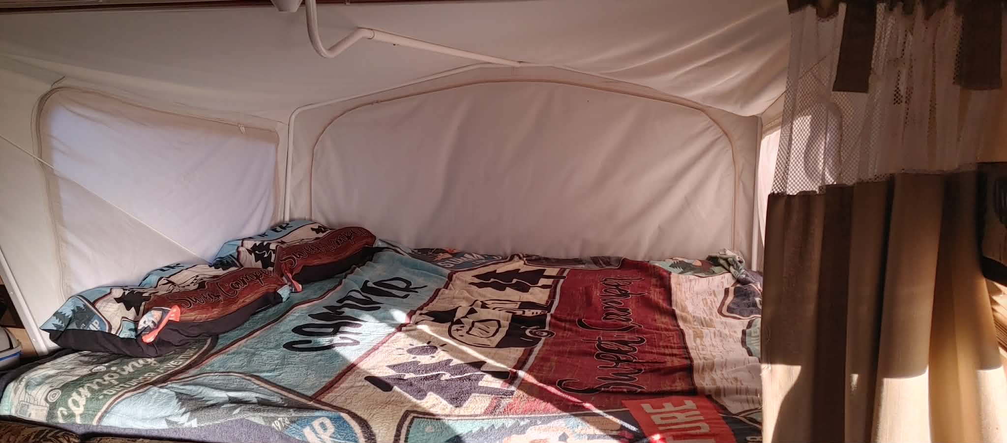 Cozy pop-up rv rental interior with camping-themed bedding. Sunlight fills the comfortable bed, ready for adventure.. Jayco Jay Feather Select EXP 2011