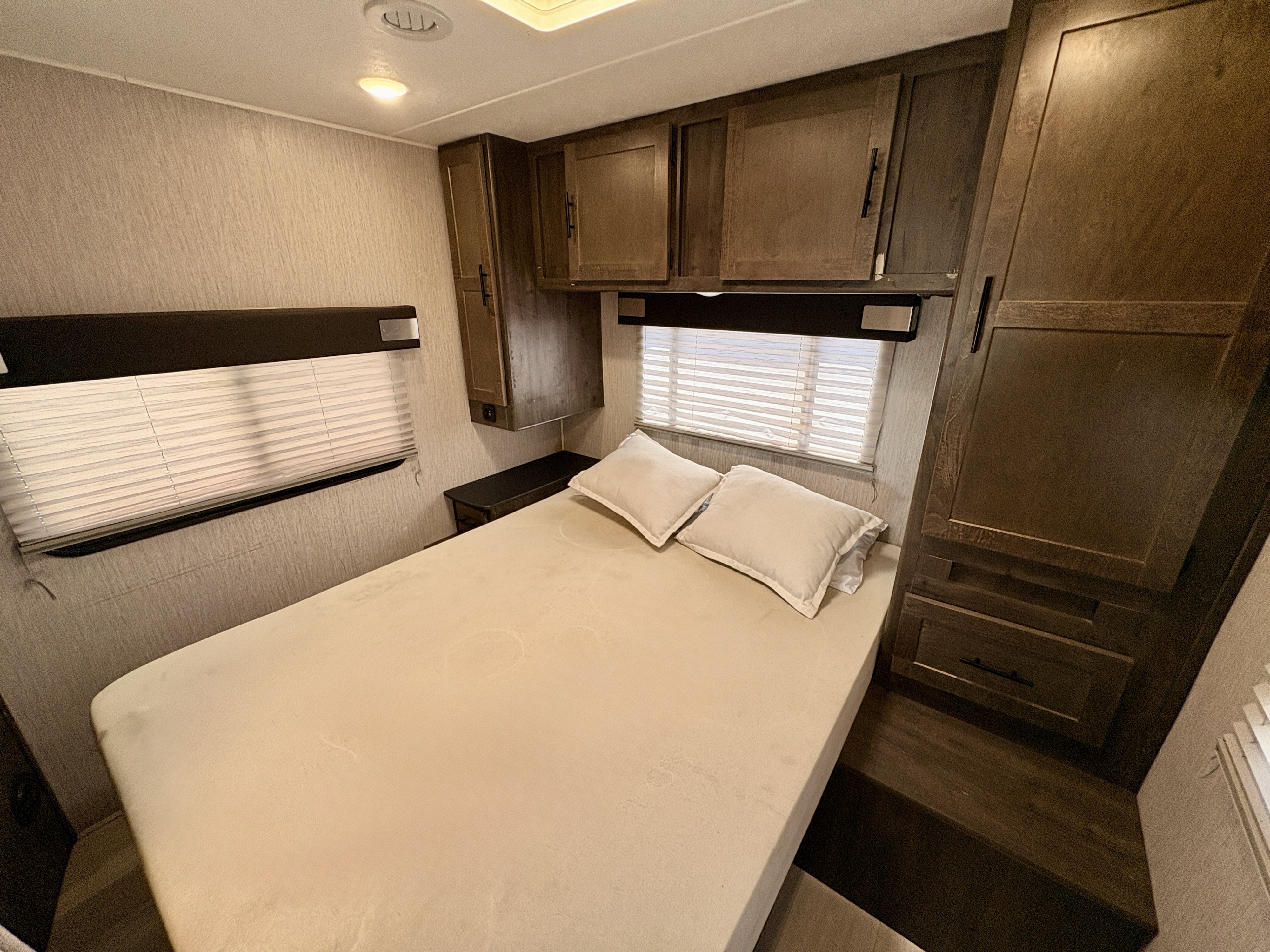 RV rental bedroom: a cozy space with a bed, overhead storage cabinets, and windows with blinds for natural light.. Forest River Coachmen Leprechaun 2021